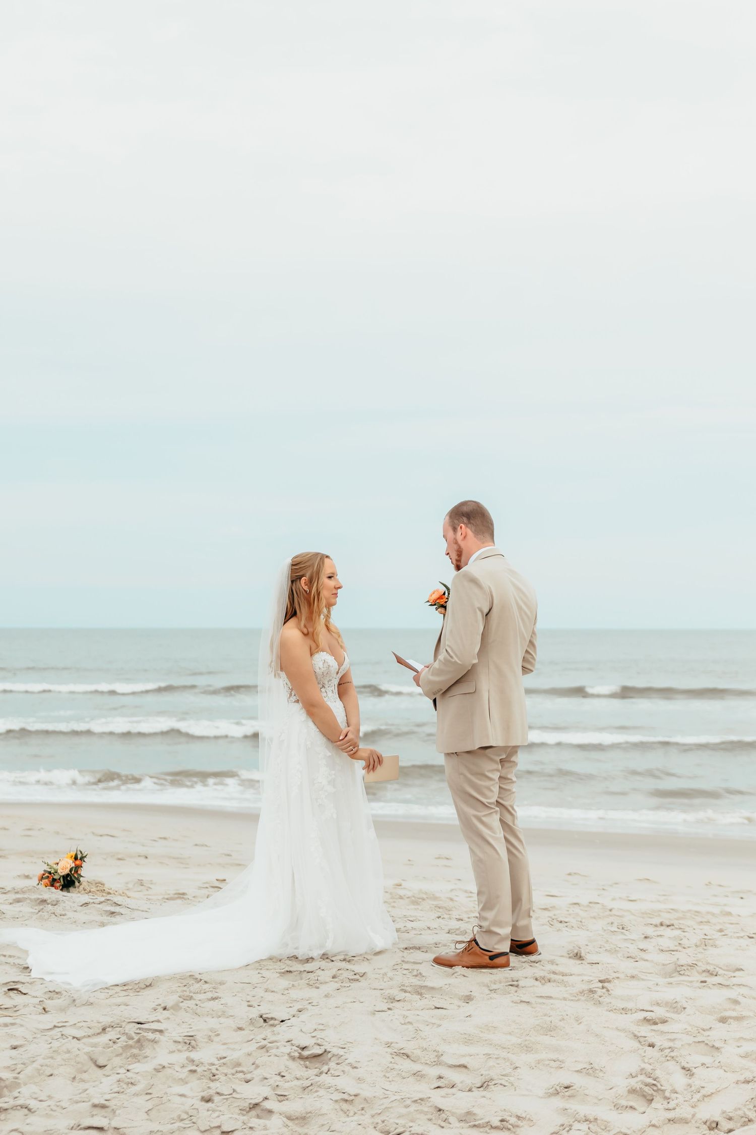 A couple shares an intimate moment during their beach wedding ceremony with waves crashing in the background.