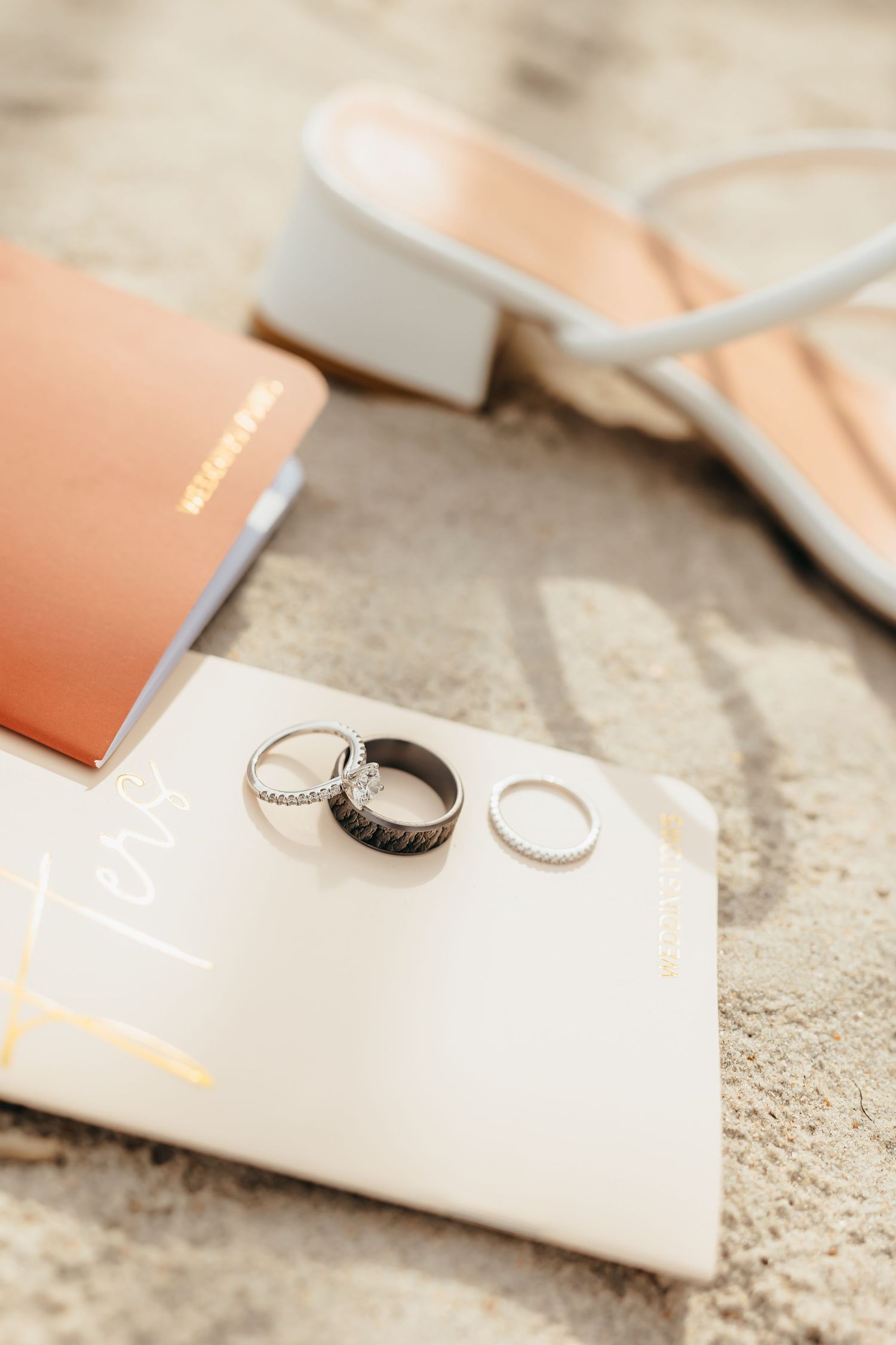 Wedding rings and jewelry displayed on white and peach colored surfaces with soft lighting and shallow depth of field.