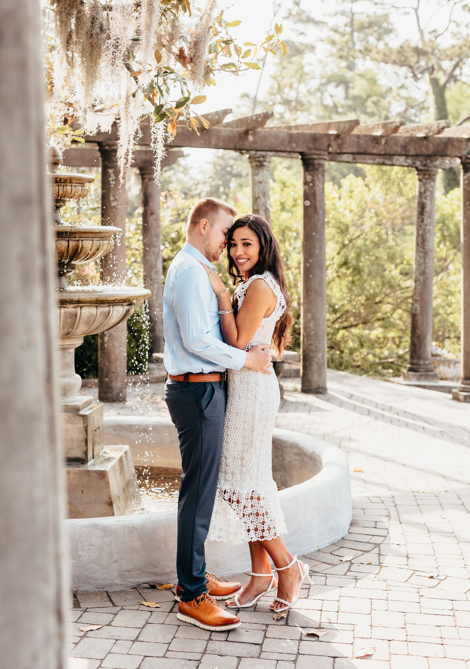 A romantic proposal moment unfolds on a stone patio surrounded by elegant columns and natural light.