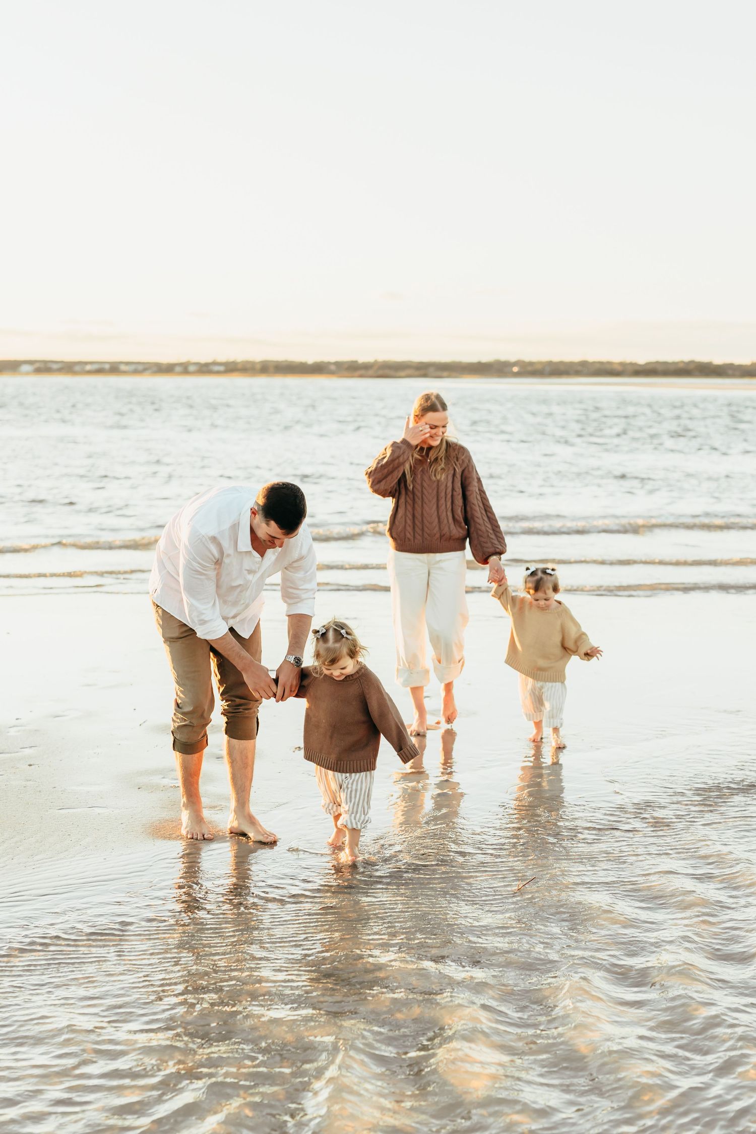 Family with golden retriever dog enjoying a beach day while wading in shallow ocean waves at sunset.