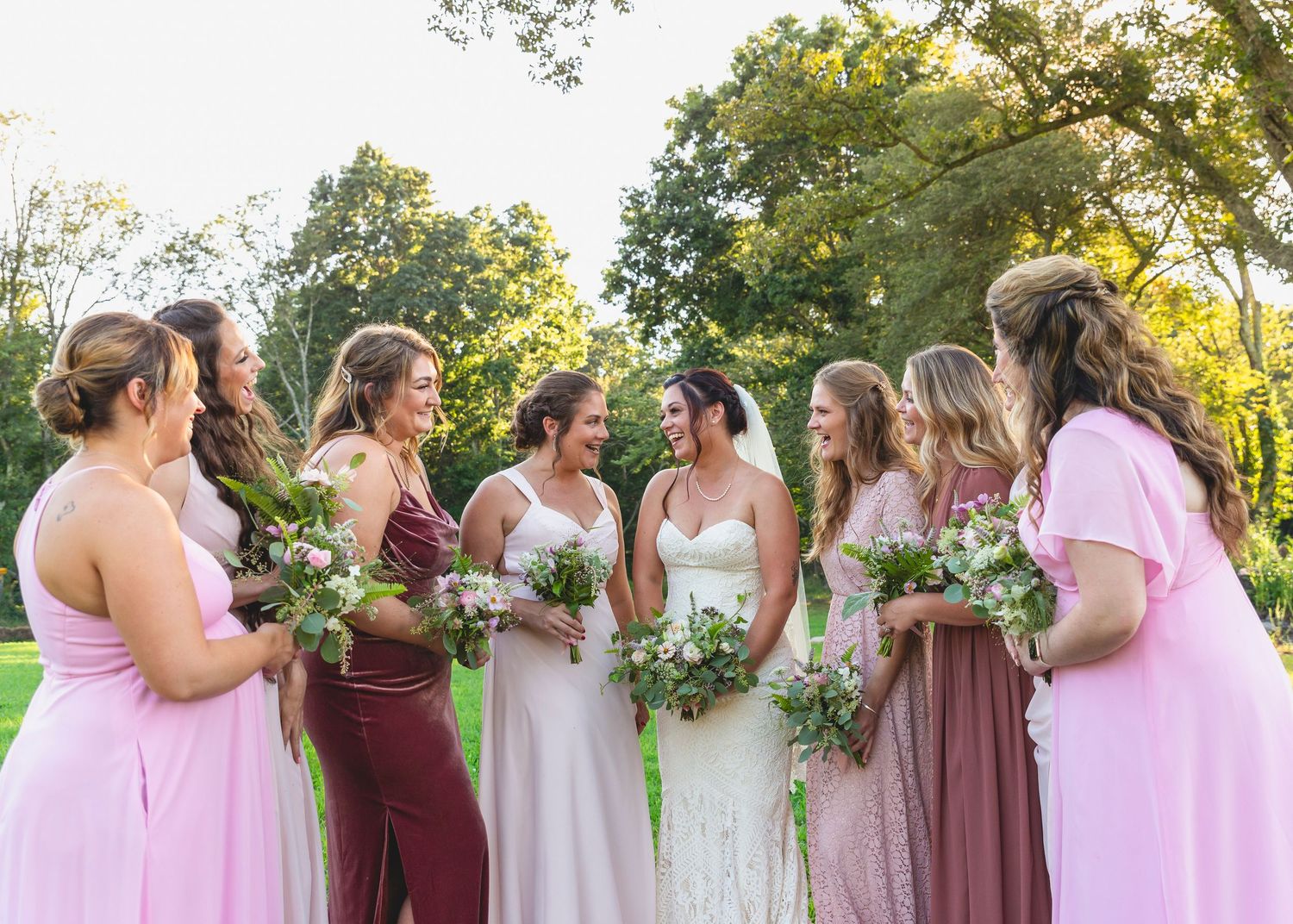 Wedding party in varying shades of pink and burgundy dresses gathered outdoors.