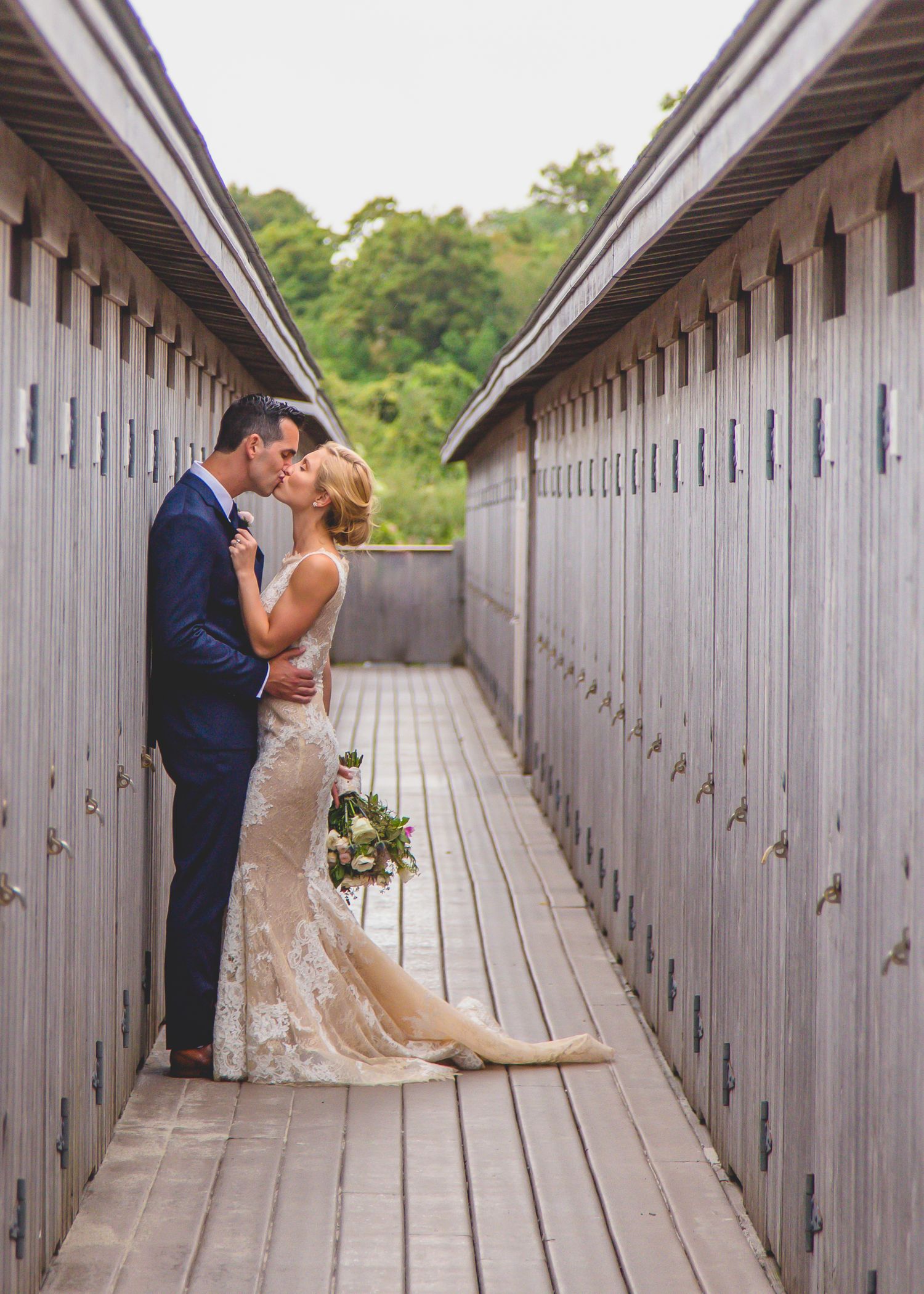 A couple shares an intimate moment on a wooden walkway between white storage units on their wedding day.
