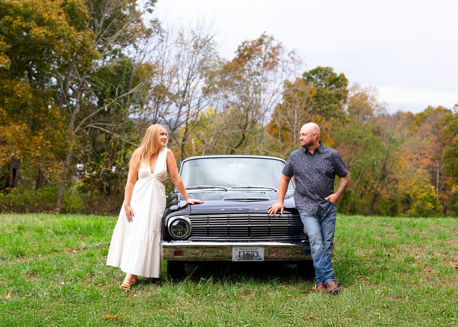 A couple poses with a classic vintage black Ford car in a fall field.