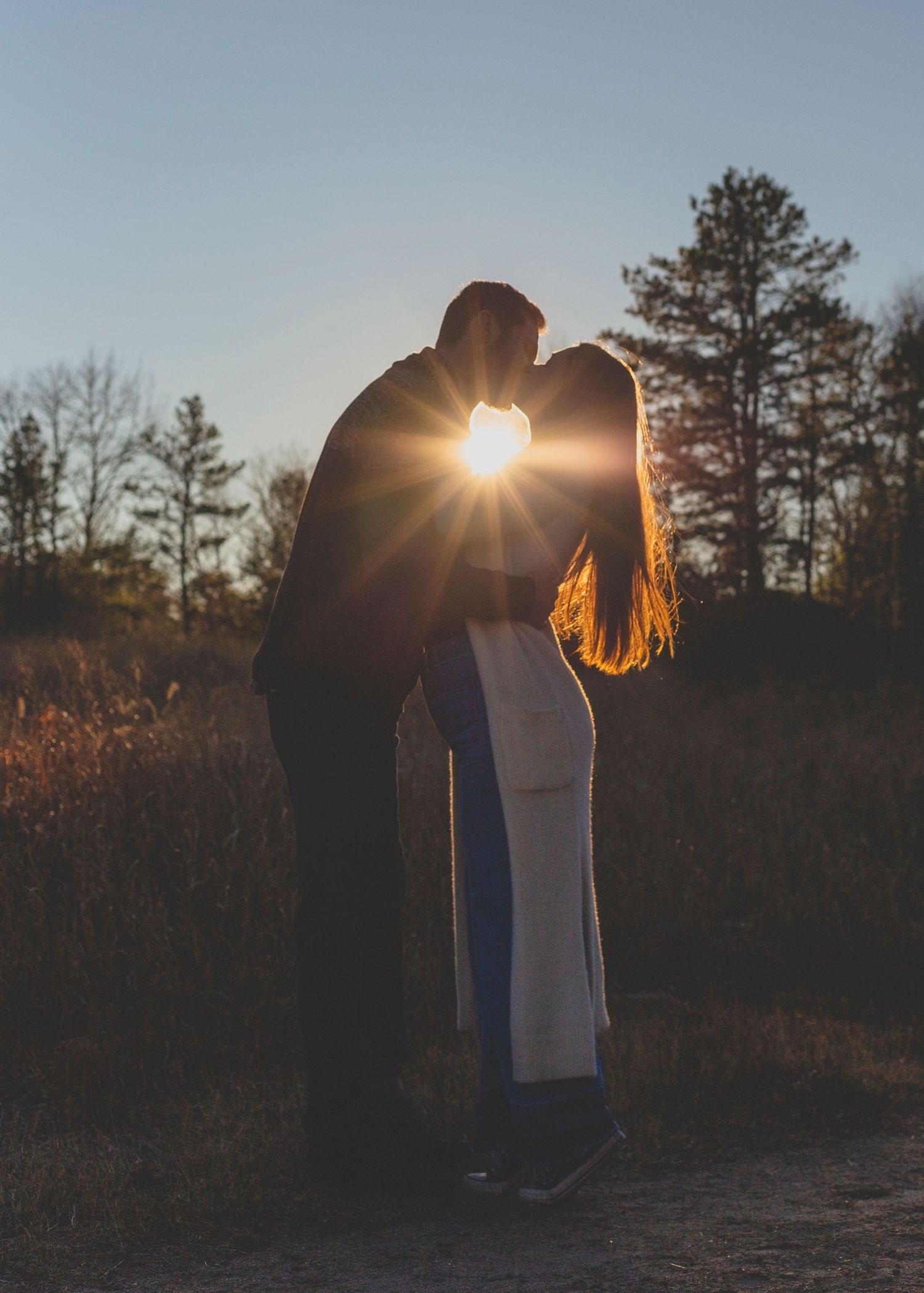 Couple in a field exchanging a kiss with sunlight shining through