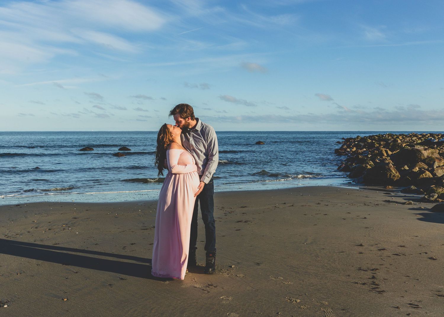 A couple embraces on a rocky beach at sunset.