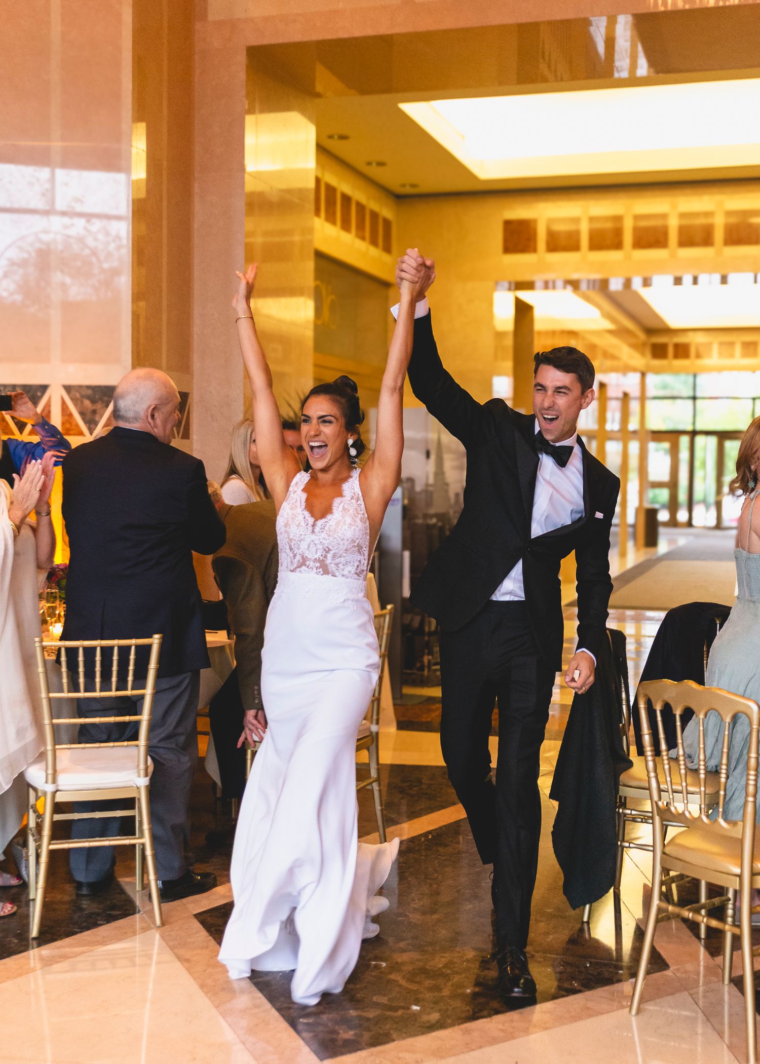Newlyweds make joyful entrance at wedding reception in elegant indoor venue.