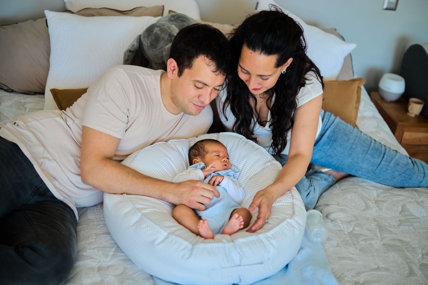 A tender moment of parent and newborn baby bonding on a white bed at home.