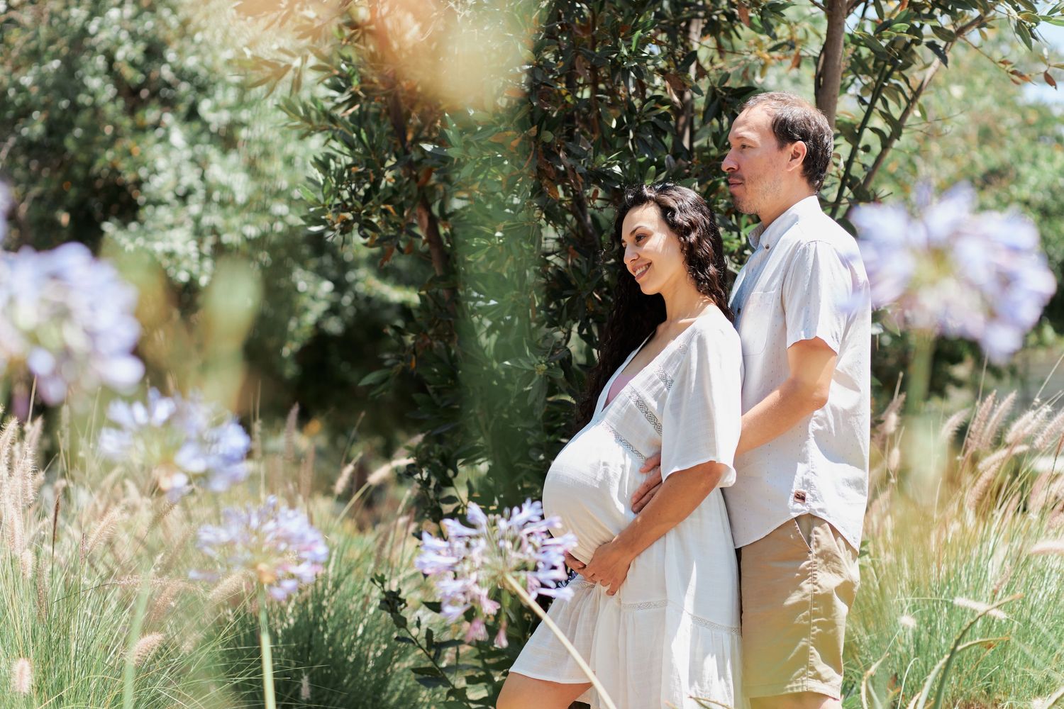 A couple embraces in a romantic outdoor setting surrounded by blooming wildflowers and trees.