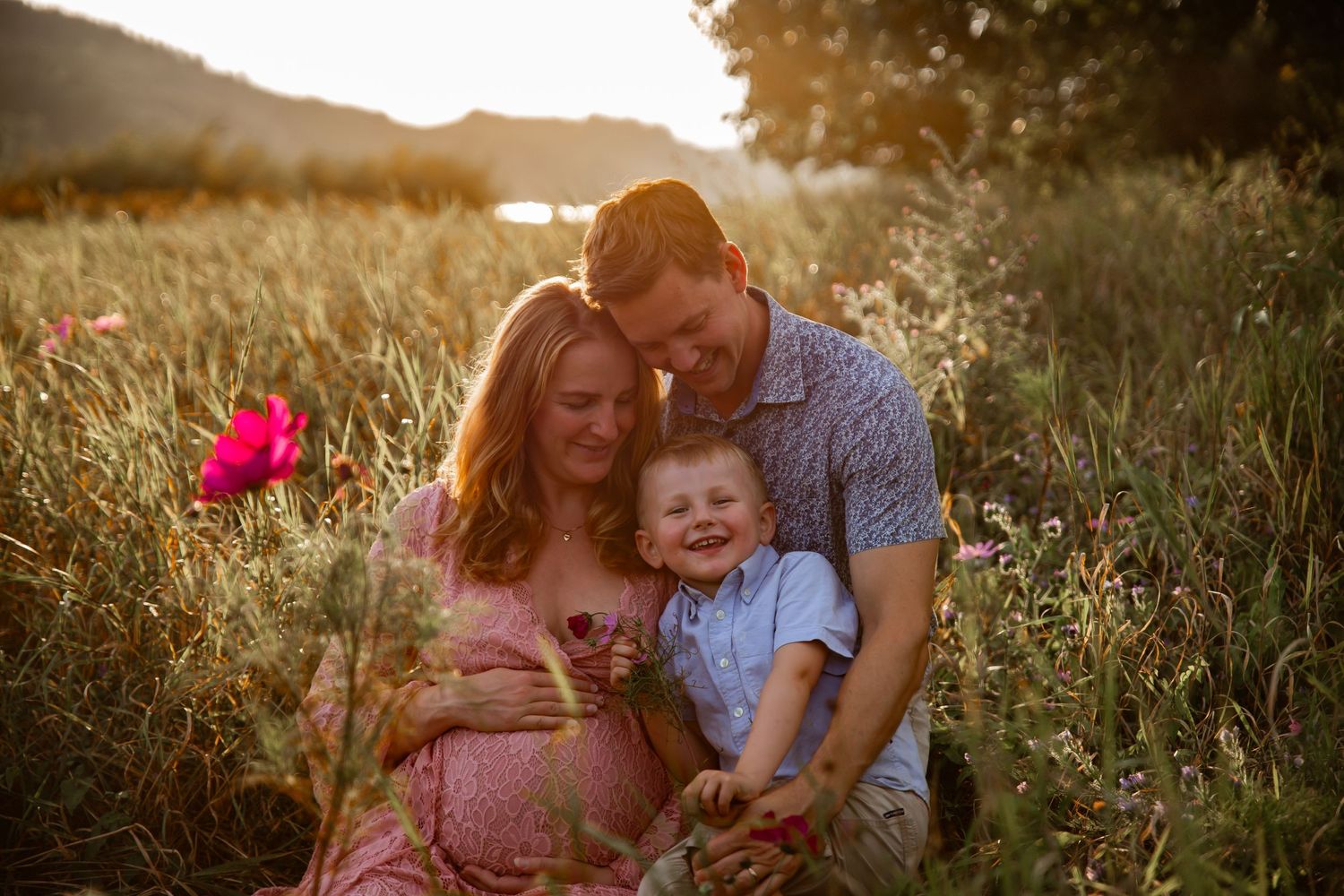 A family shares a tender moment together in a sunlit summer field with wildflowers at golden hour.