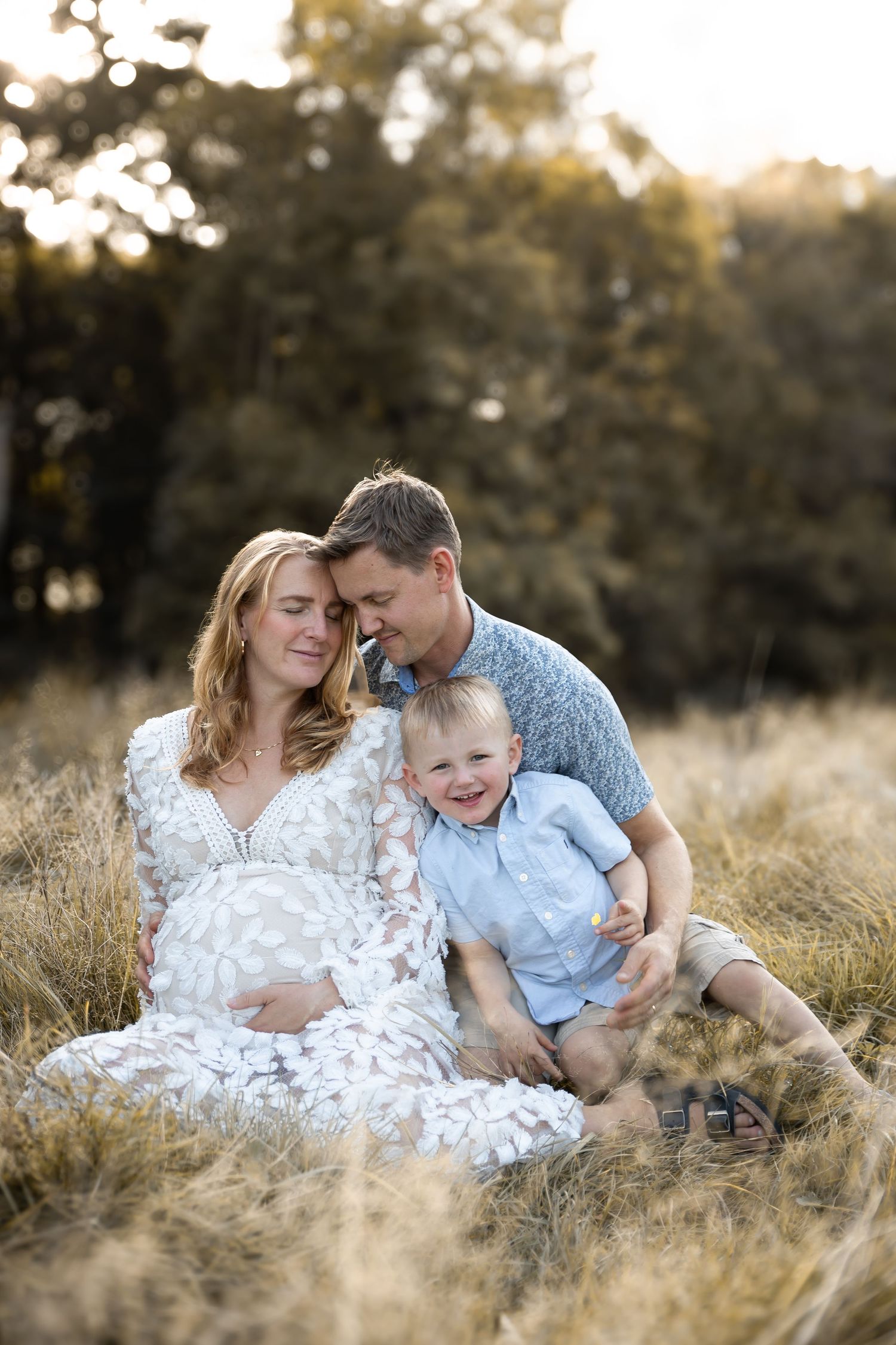 A family sits together in a golden grass field at sunset sharing an intimate moment.