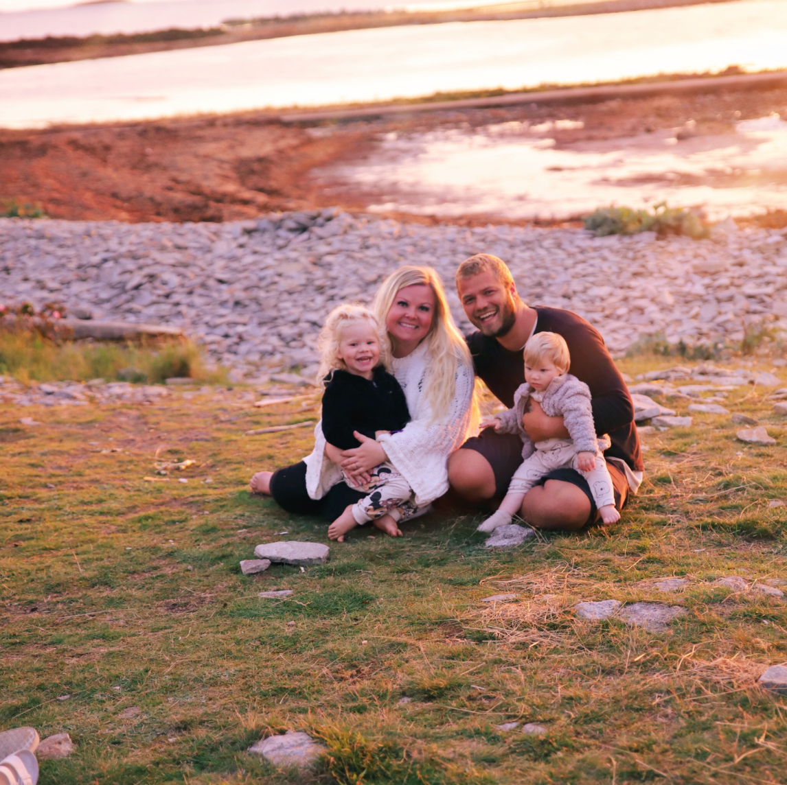 Family enjoying a playful moment together while sitting on a grassy hillside during sunset.