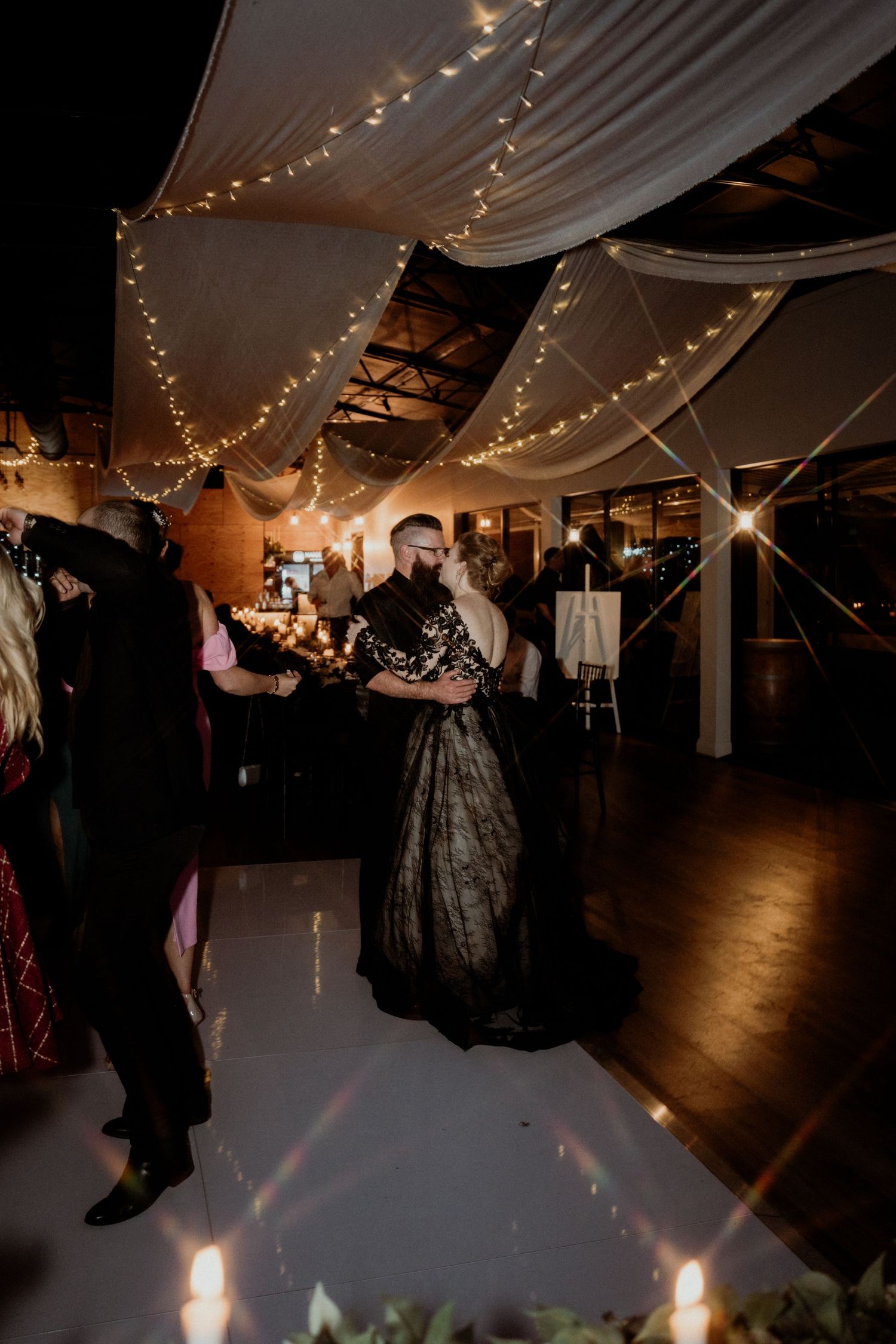 Couple shares first dance at elegant wedding reception with fairy lights and draped ceiling decor in dimly lit venue.