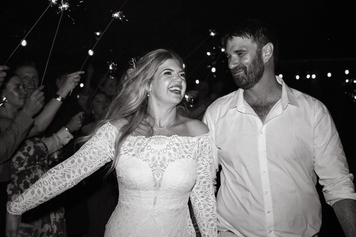 Bride and groom walking through a sparkler exit tunnel, smiling joyfully in black and white photo.