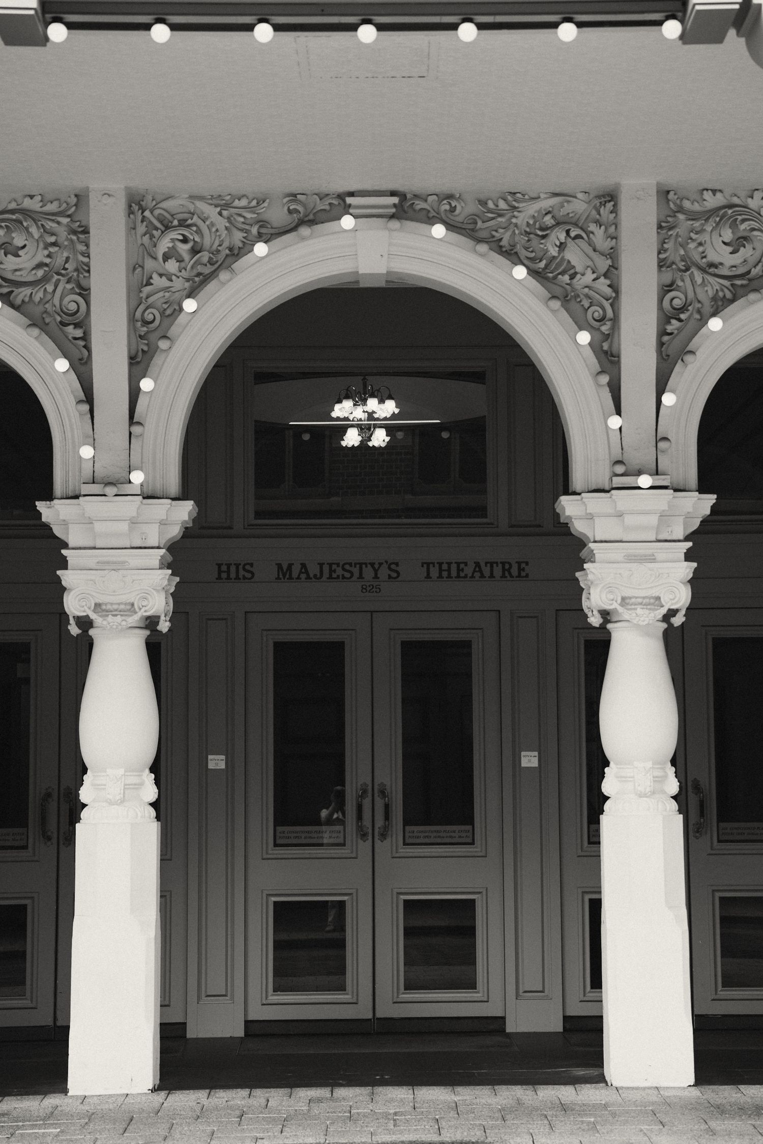Classical white columns and arches line the entrance of His Majesty's Theatre in black and white architectural detail.