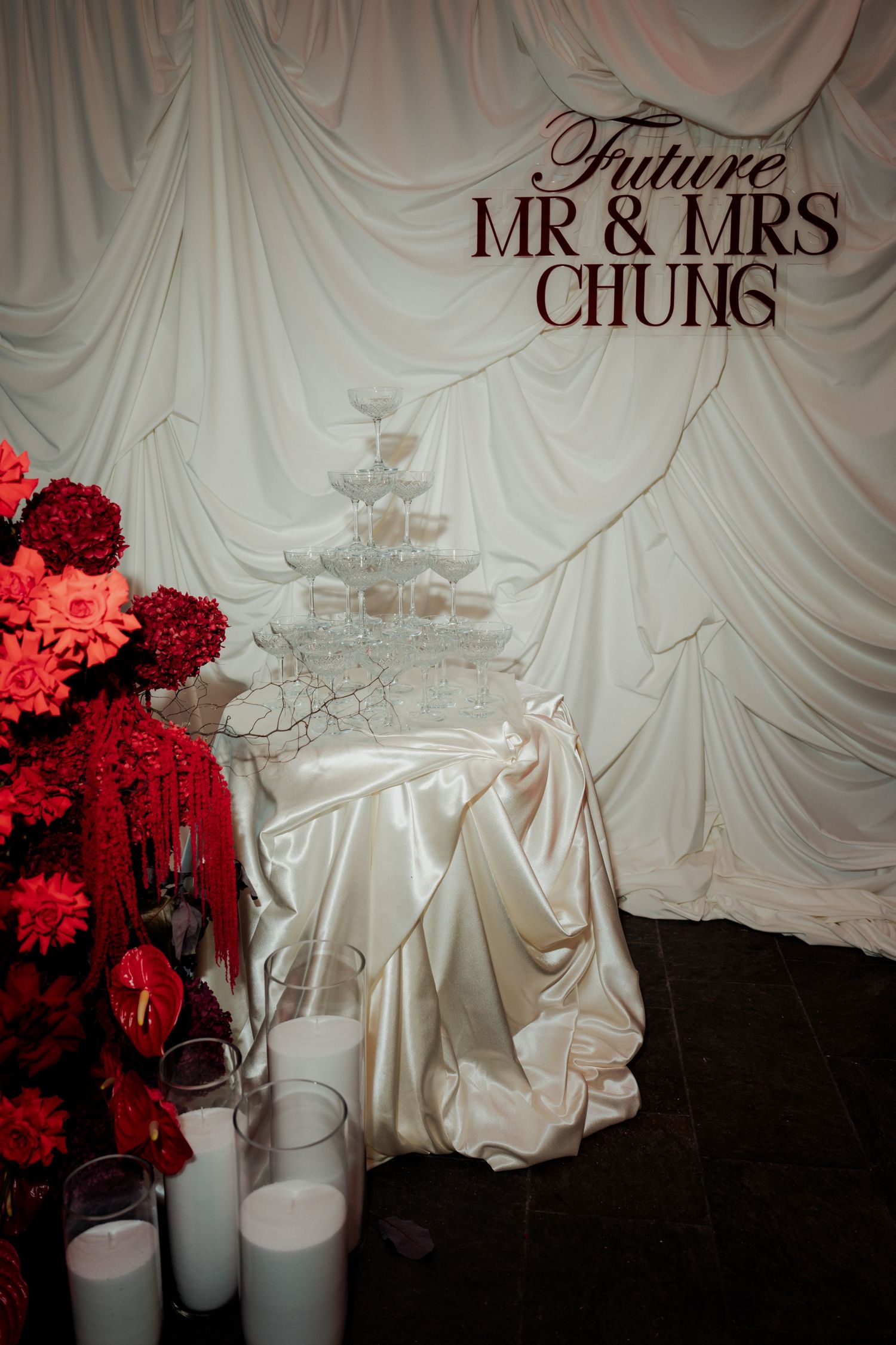 Elegant wedding champagne tower display with red floral arrangements and Future Mr & Mrs Chung signage on draped white backdrop.