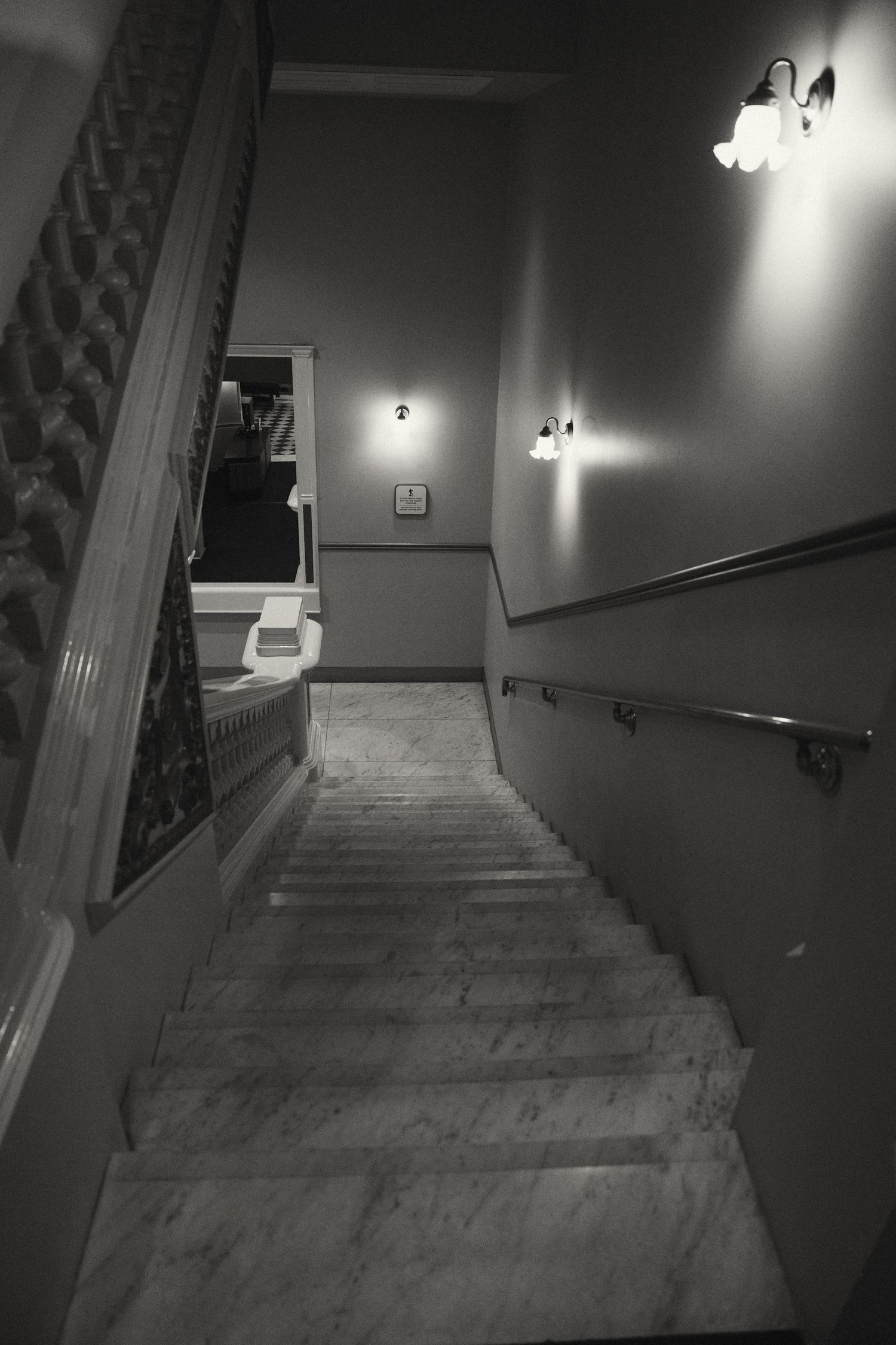 Dark black and white surveillance camera footage shows descending stairs and hallway with eerie lighting and wall fixtures.
