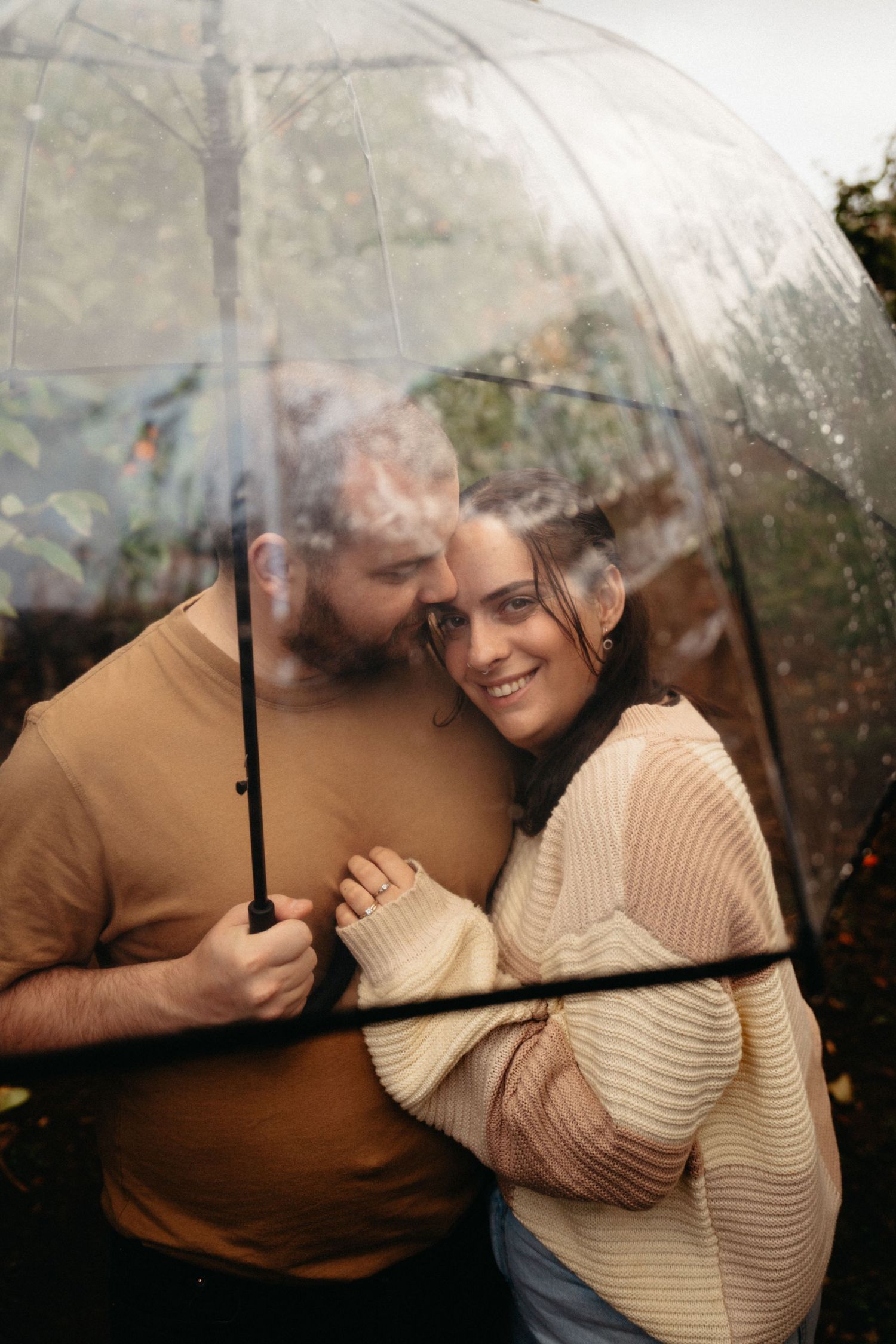 A couple laughing together under a clear umbrella on a rainy autumn day.