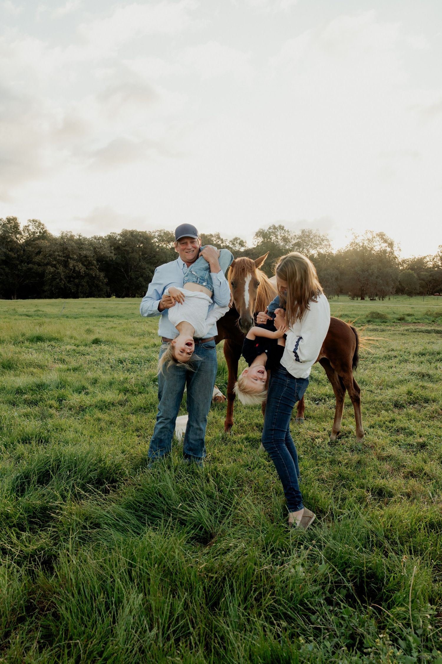 Family with two children and a horse playing in a green field at sunset on a farm.