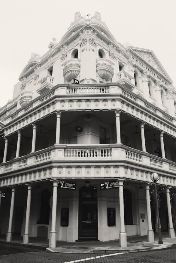 Black and white photograph of a historic Victorian corner building with ornate balconies and decorative columns in architectural detail.
