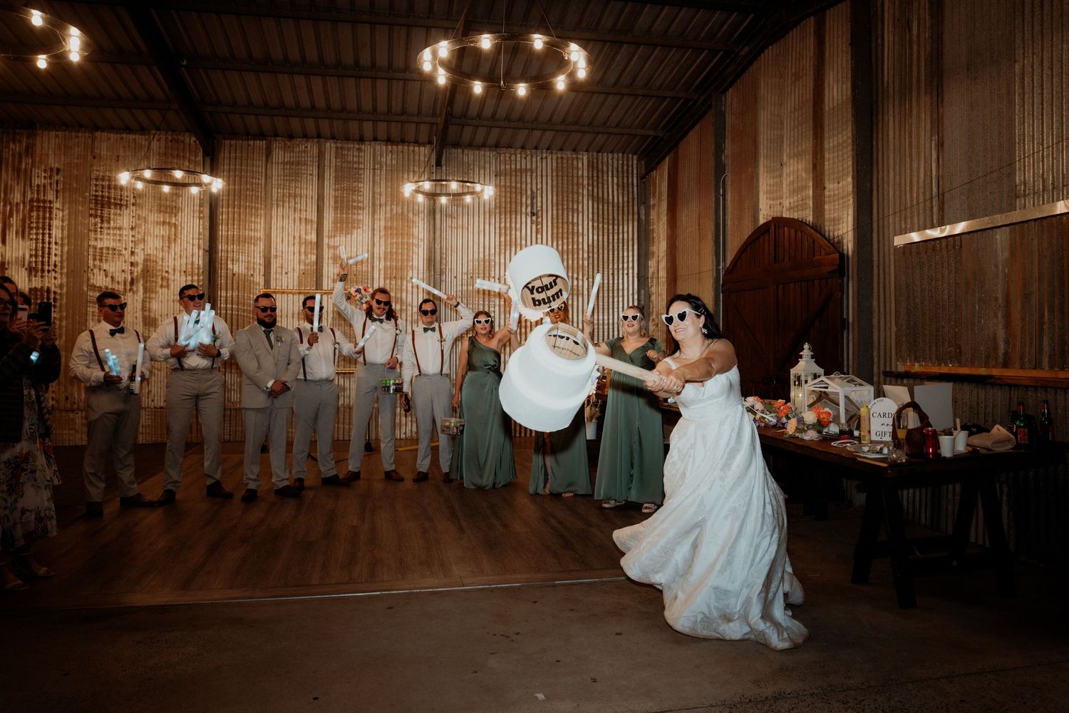 Bride dances with costumed character at rustic barn wedding reception while groomsmen and bridesmaids watch.