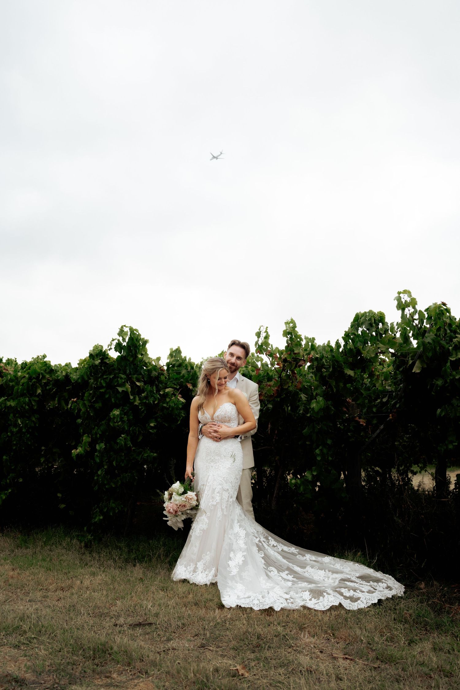 Bride and groom embracing in front of lush vineyard rows on their wedding day.