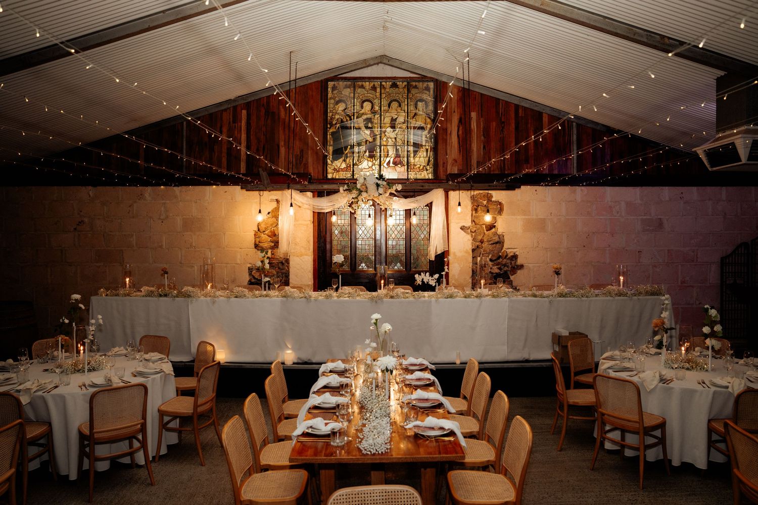 An elegant wedding reception venue with vaulted ceiling, warm lighting and formal table settings.