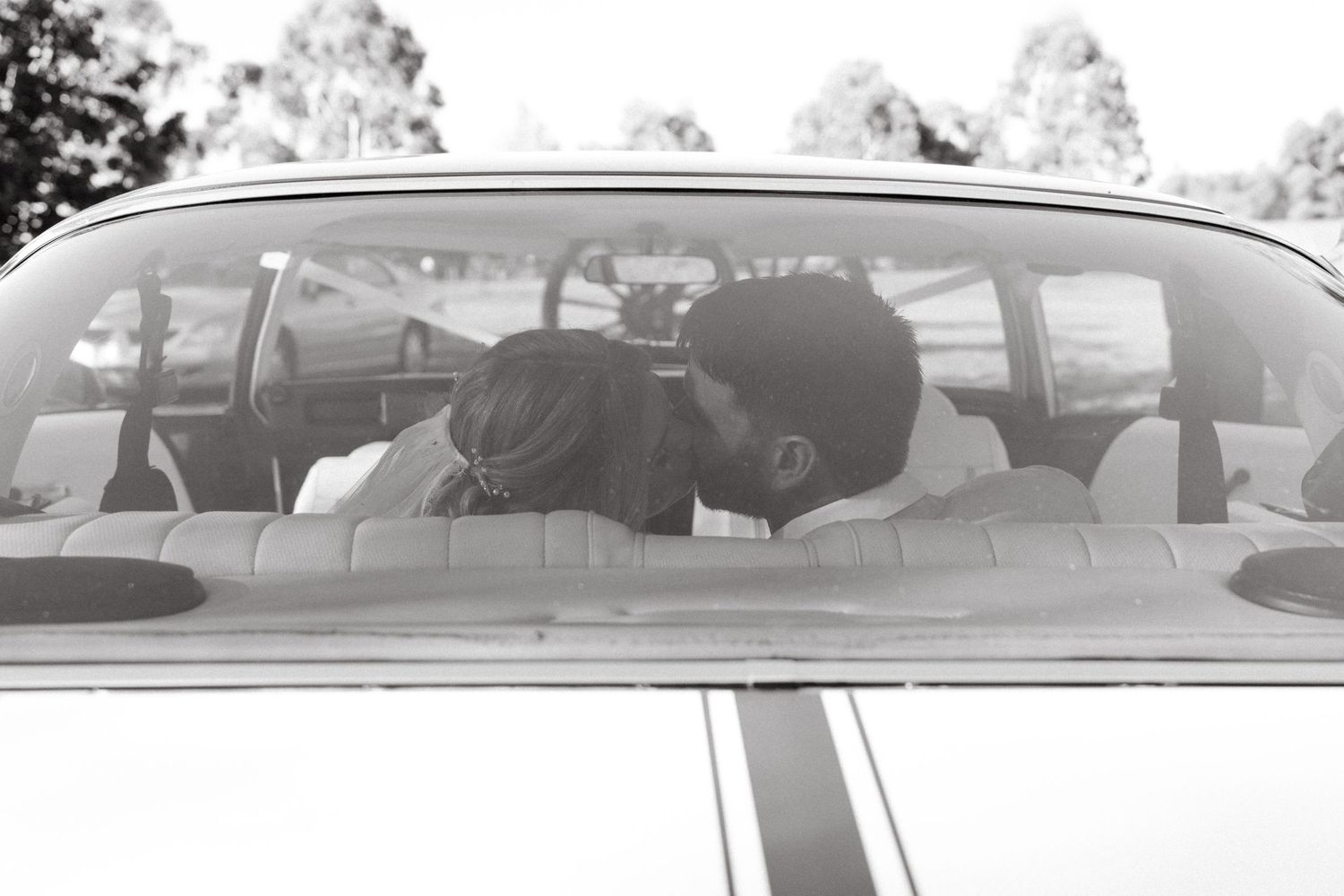 Couple sharing a romantic kiss inside a vintage car, captured in black and white photography.