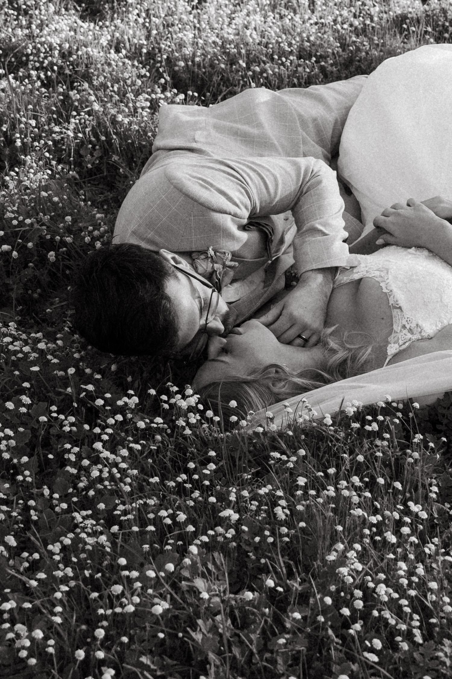Black and white photo of a couple kissing while lying in a field of wildflowers.