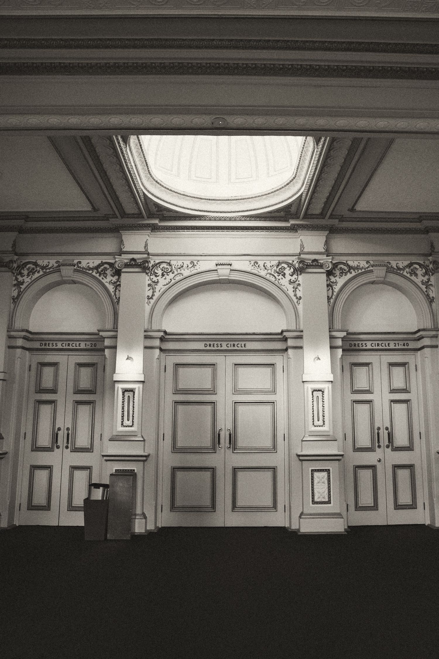 Black and white interior architectural photograph showing classical wall panels and ceiling with elegant round skylights.