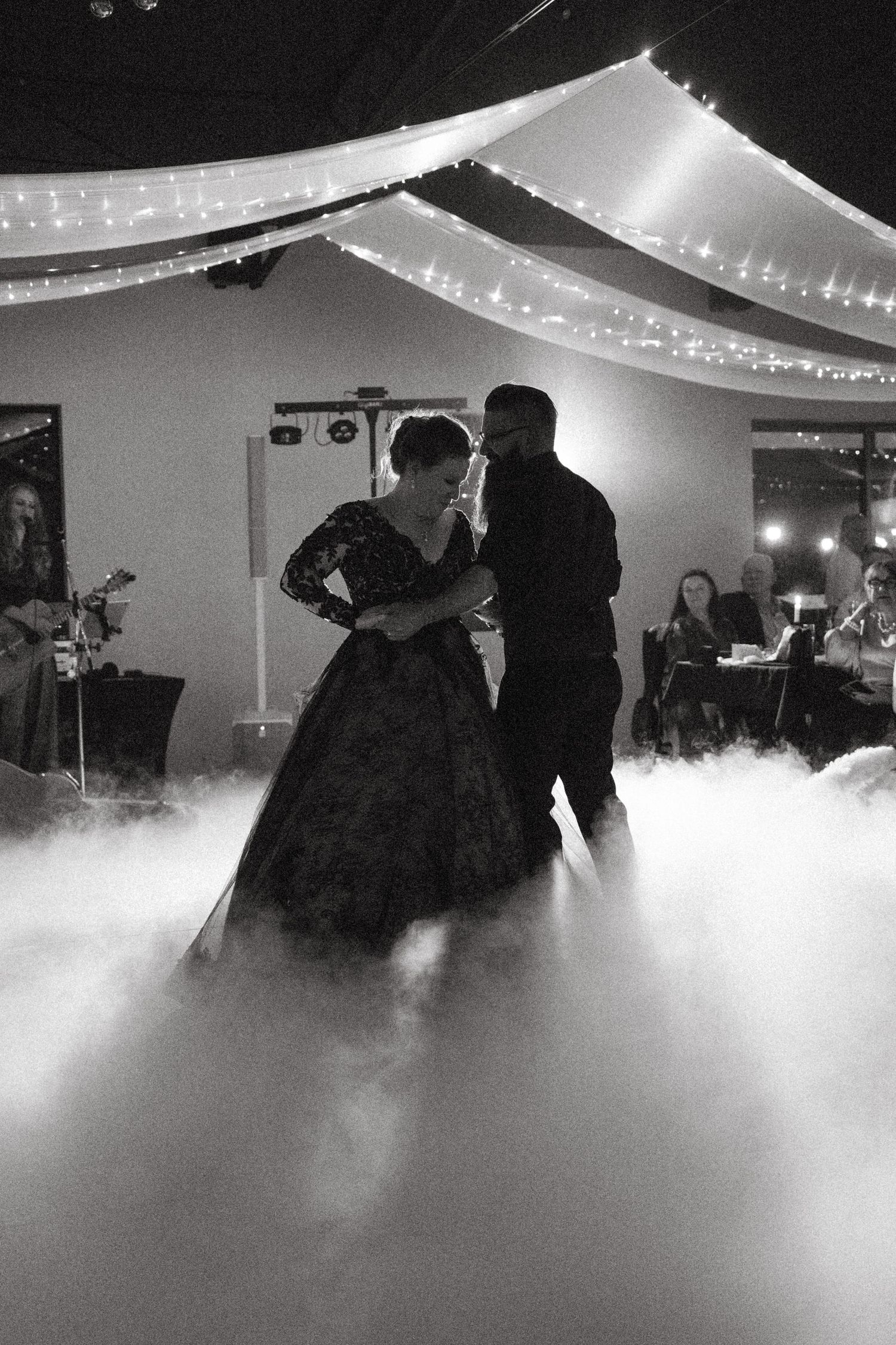 Couple shares first dance surrounded by dramatic fog at a romantic wedding reception with fairy lights.