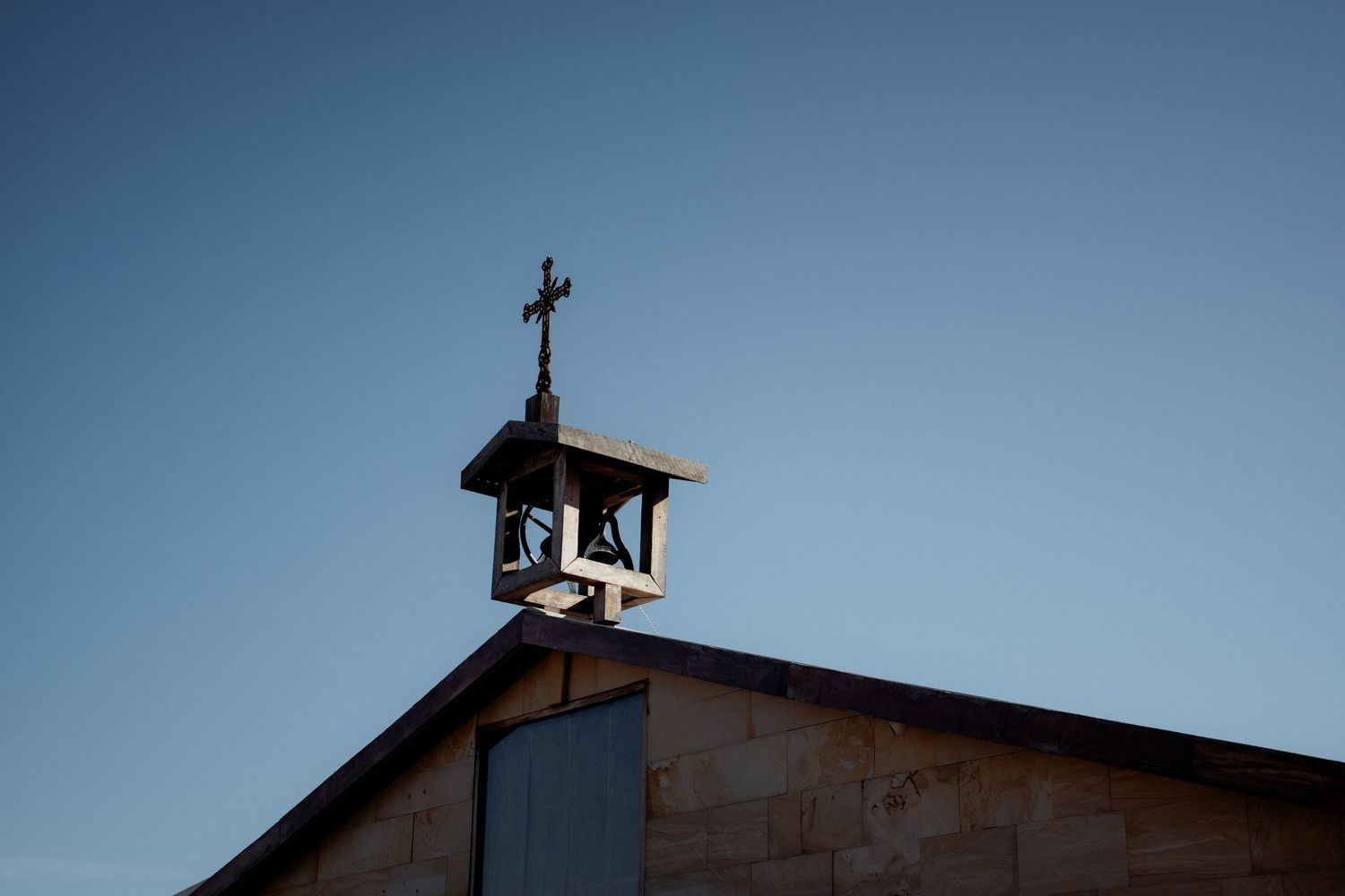 A church steeple with a cross silhouetted against a clear blue sky during daytime.