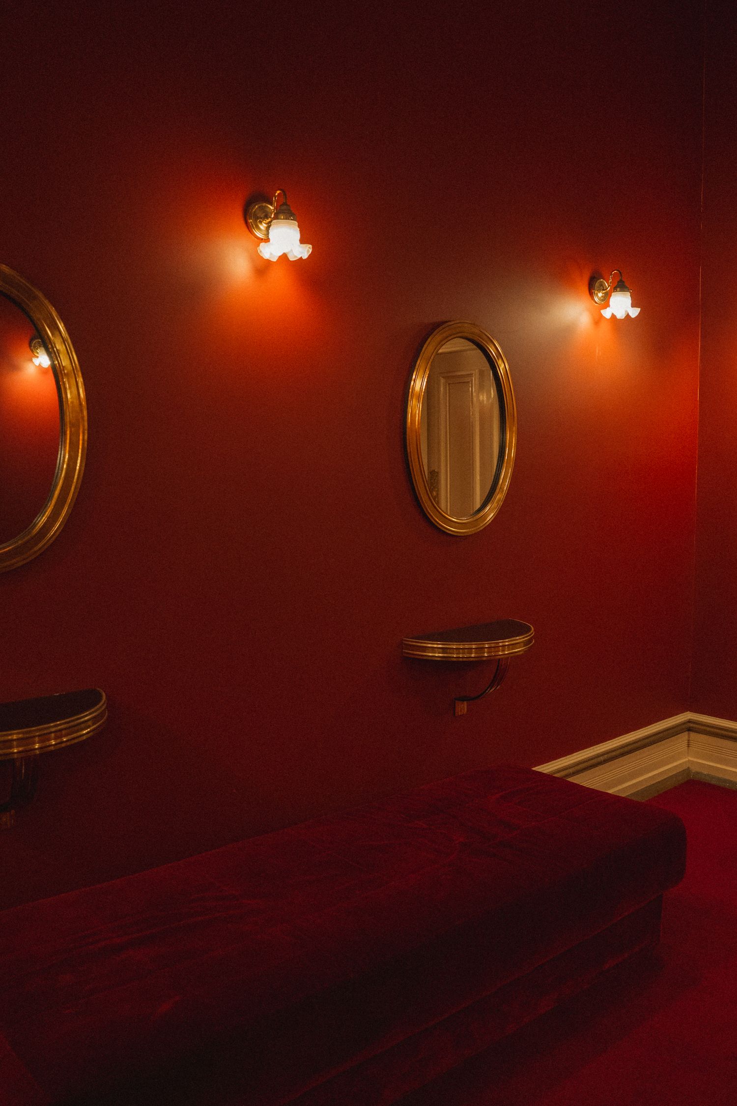 Red hallway with vintage gold mirror and dim lighting creates dramatic atmosphere in interior space.