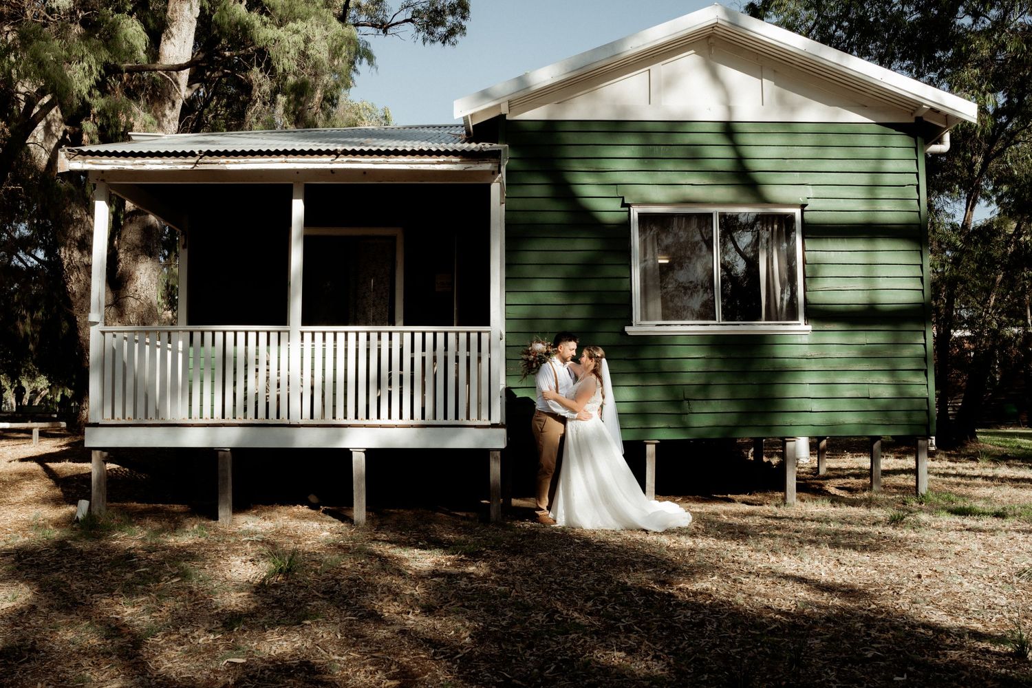 Bride and groom embracing outside a charming green wooden cottage surrounded by trees.