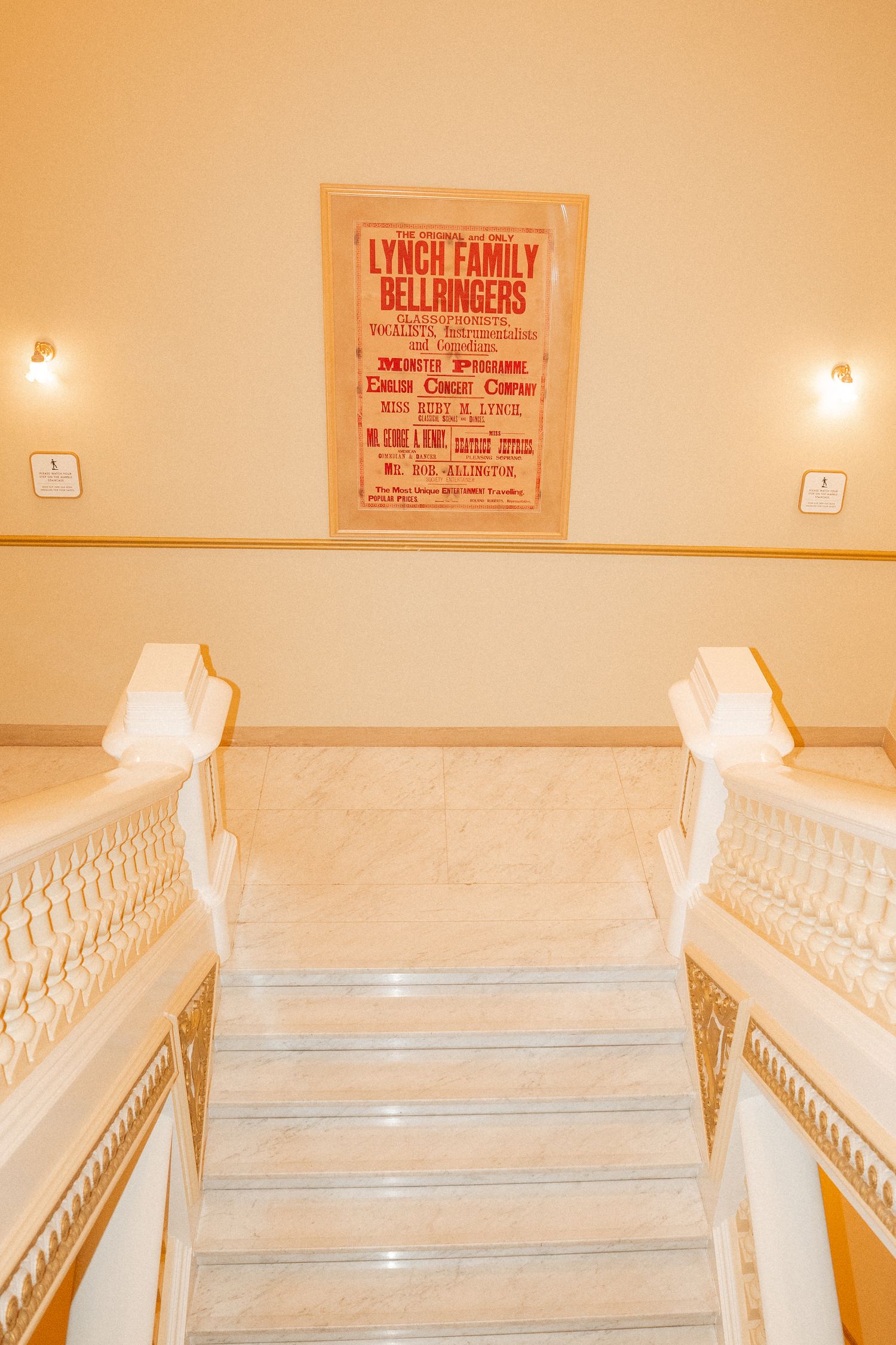 Three ornate white caskets are displayed in a funeral home with signage and beige walls.
