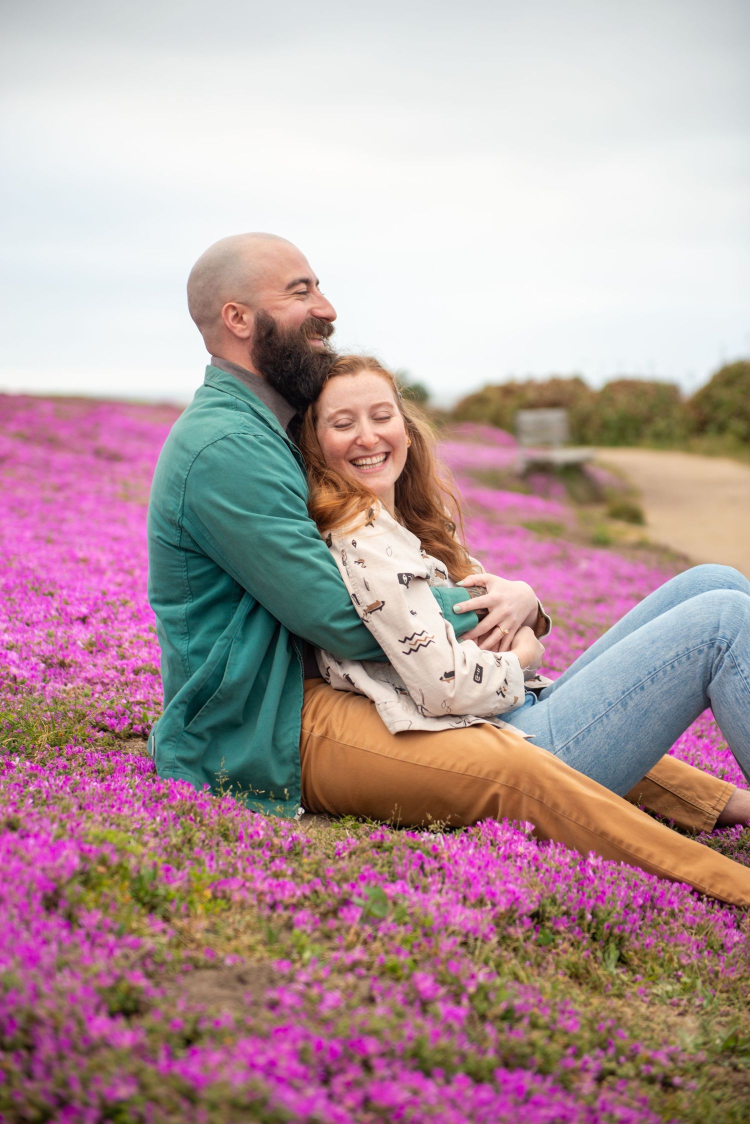 A couple lounges together in a vibrant field of pink wildflowers on a sunny afternoon.