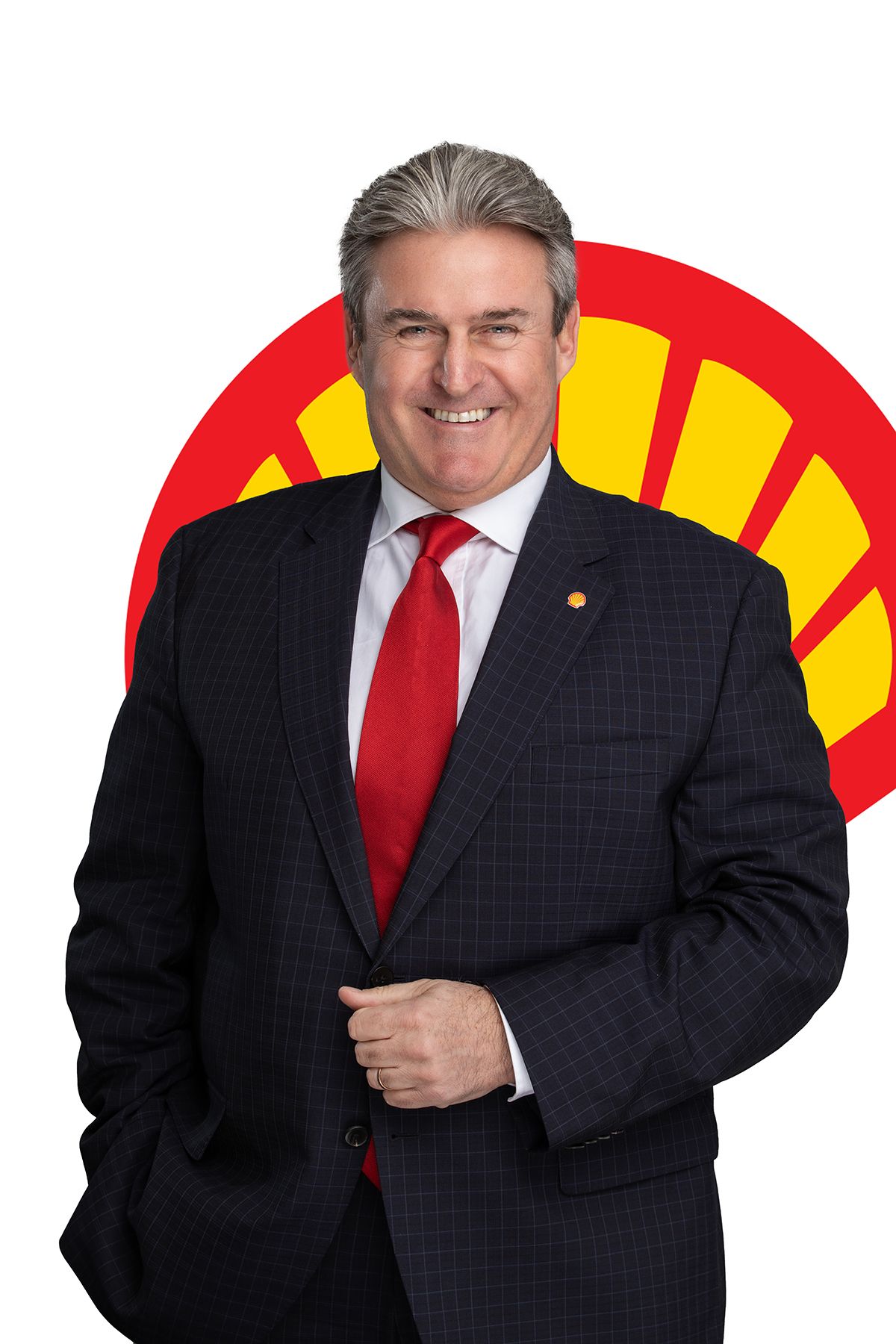 Professional business executive in navy suit and red tie poses in front of Shell oil company logo.