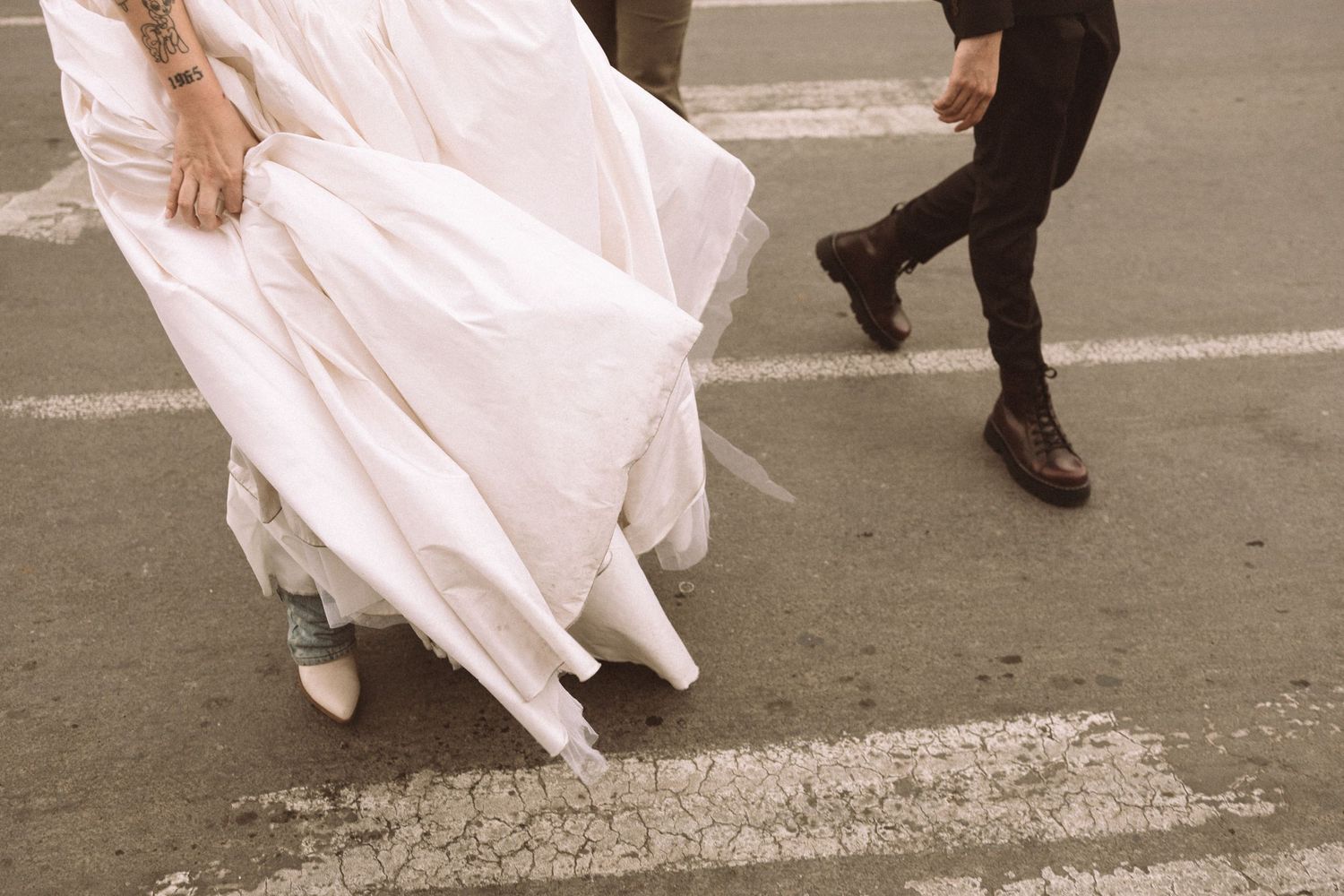 Close-up of flowing white wedding dress and dress shoes walking on pavement.