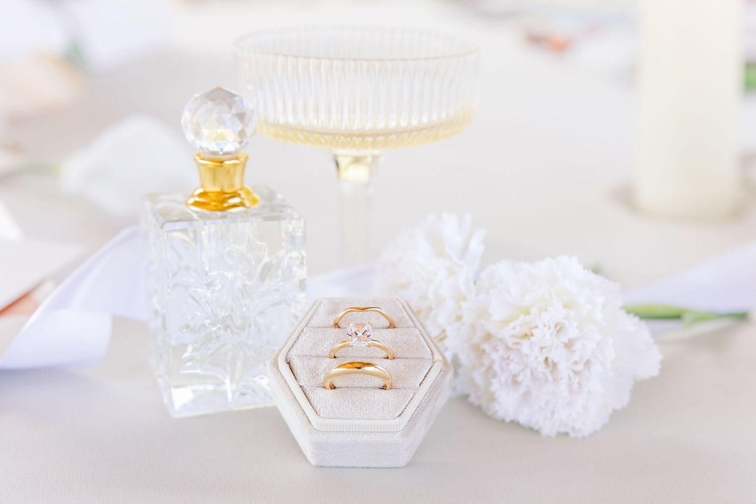 Elegant perfume bottles and white flowers arranged on a light surface in soft, dreamy lighting.