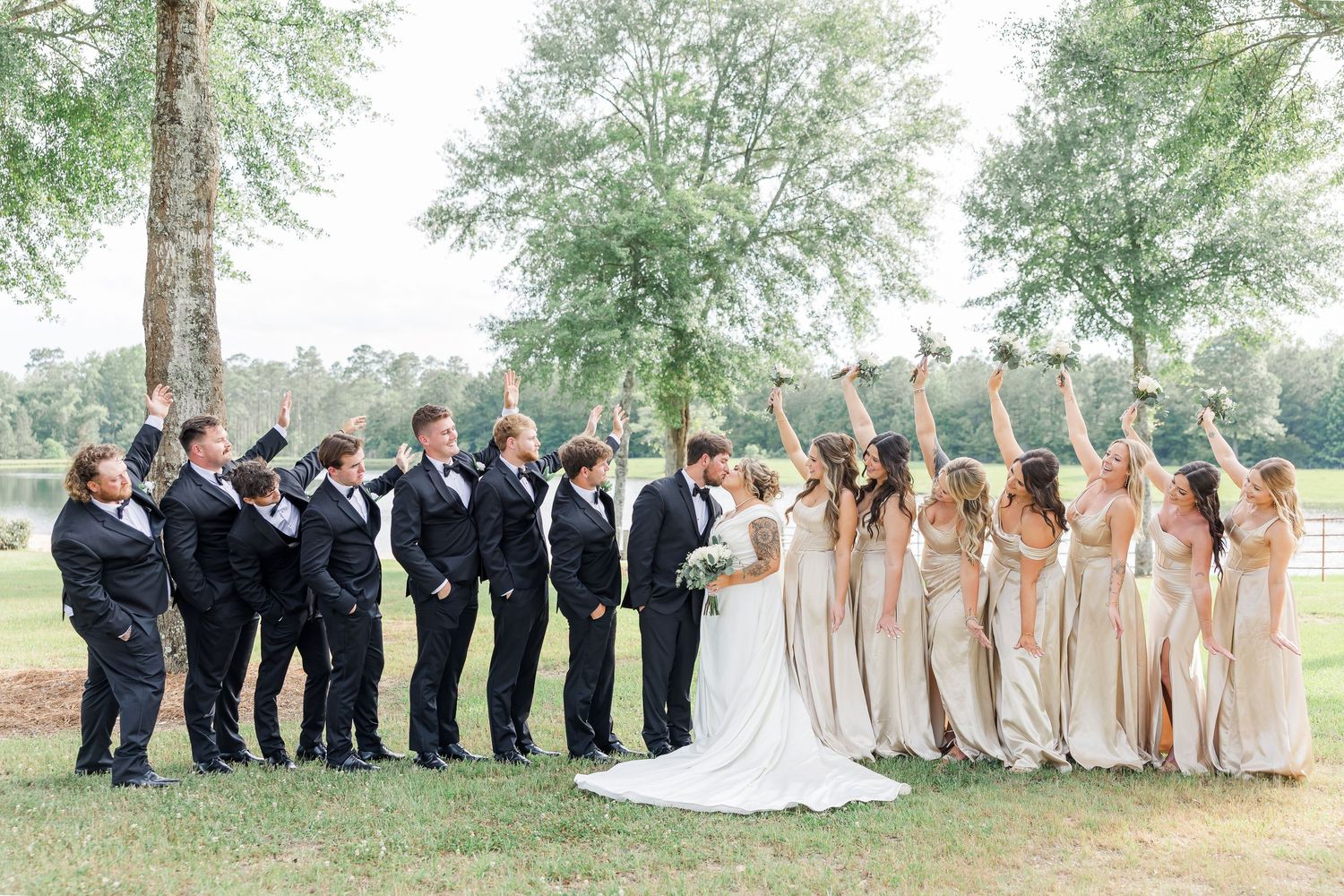 Wedding party poses in a row outdoors with bridesmaids in champagne dresses and groomsmen in dark suits.