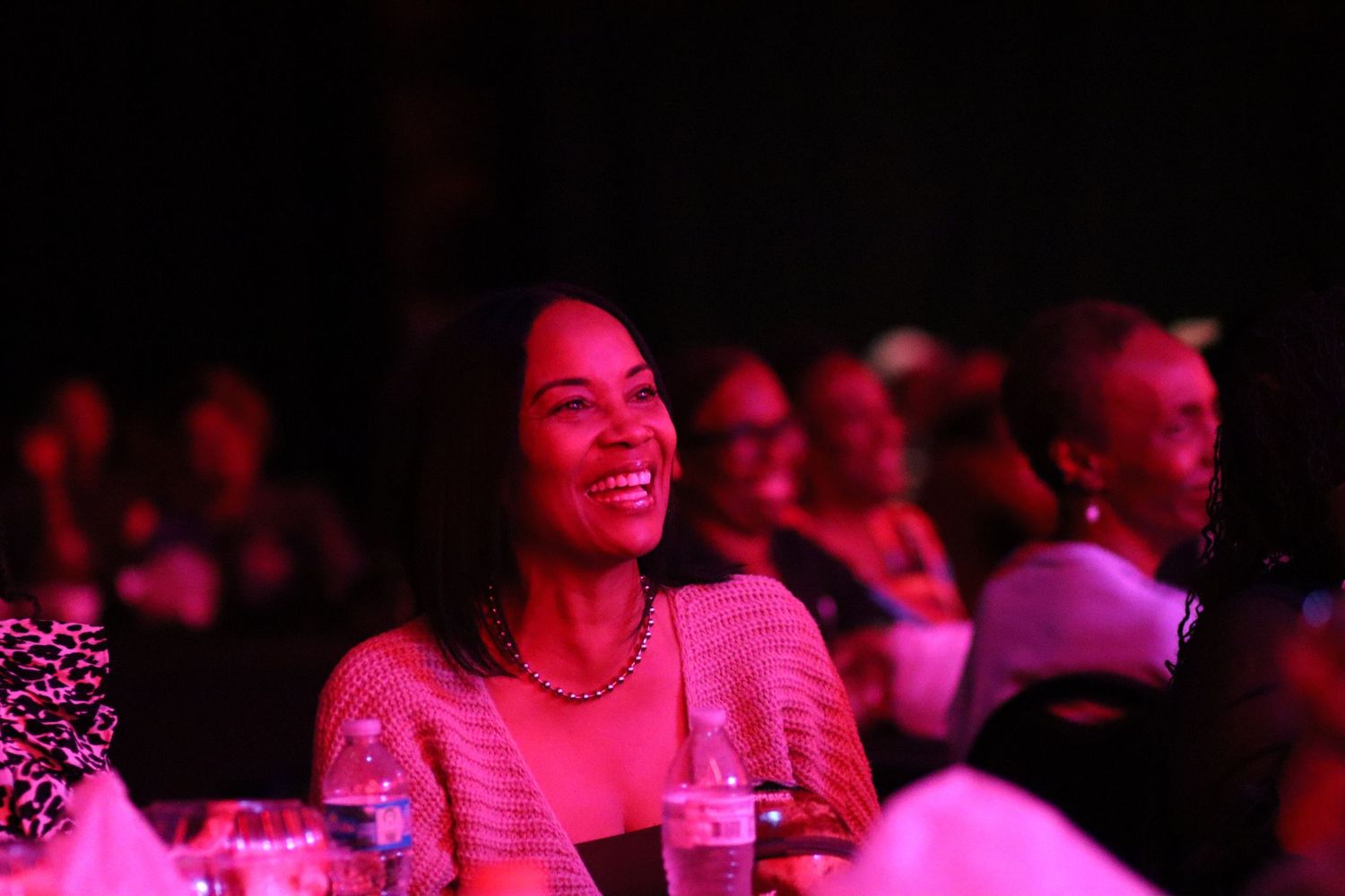 Smiling woman enjoying a live performance under pink lighting at an indoor event.