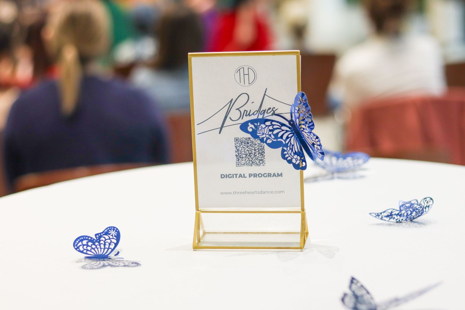Elegant table decoration featuring blue butterfly cutouts and a digital program sign in a gold frame.