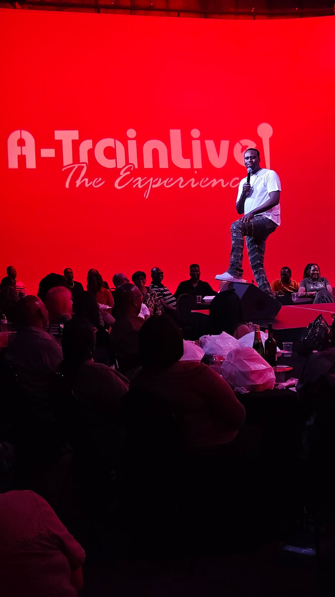 Comedian standing on stage before a large crowd at A-Train Live The Experience event.