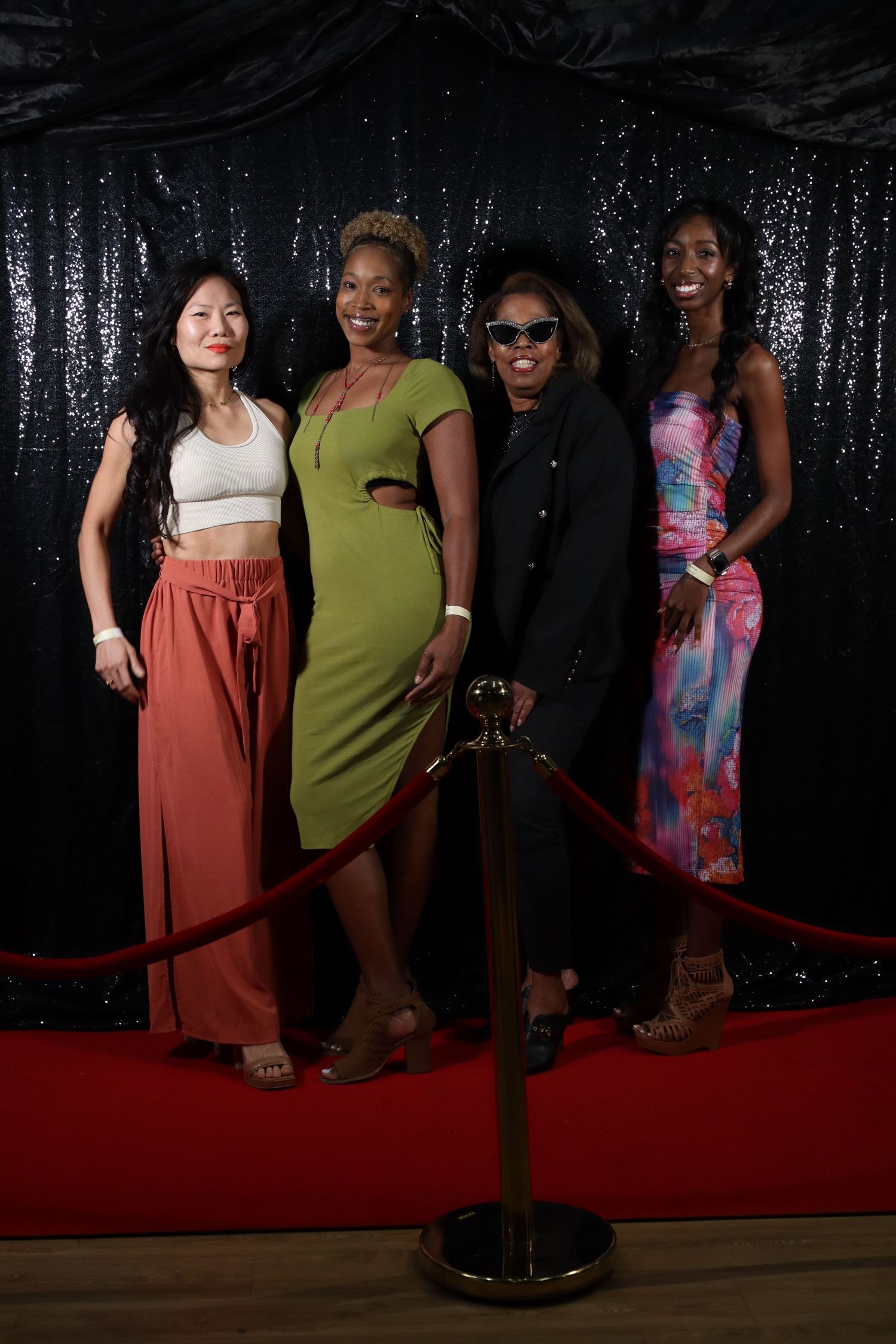 Four stylish women pose together on red carpet at glamorous evening event.