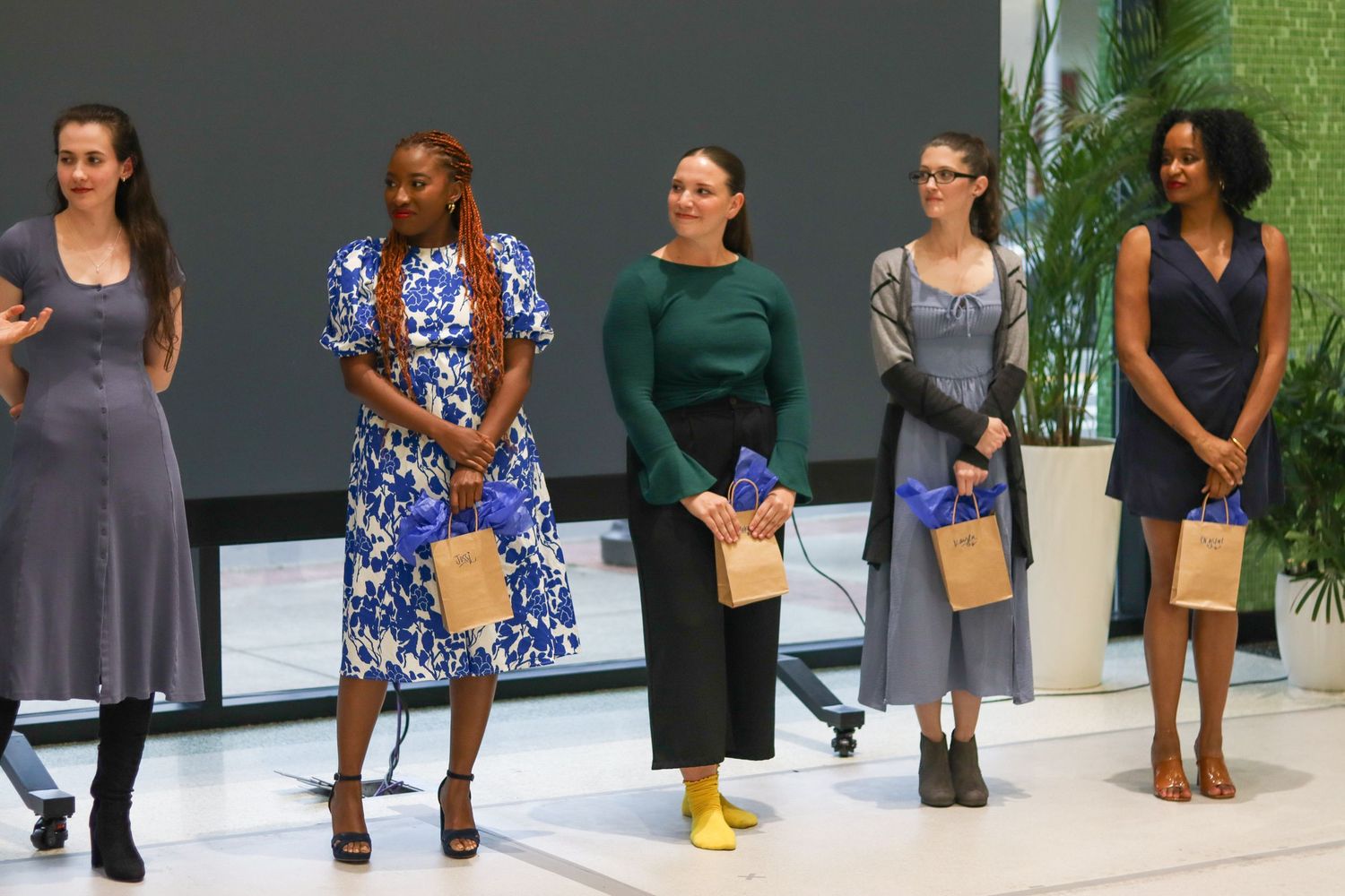 Five women in elegant dresses stand on stage receiving recognition at Bridges awards event.