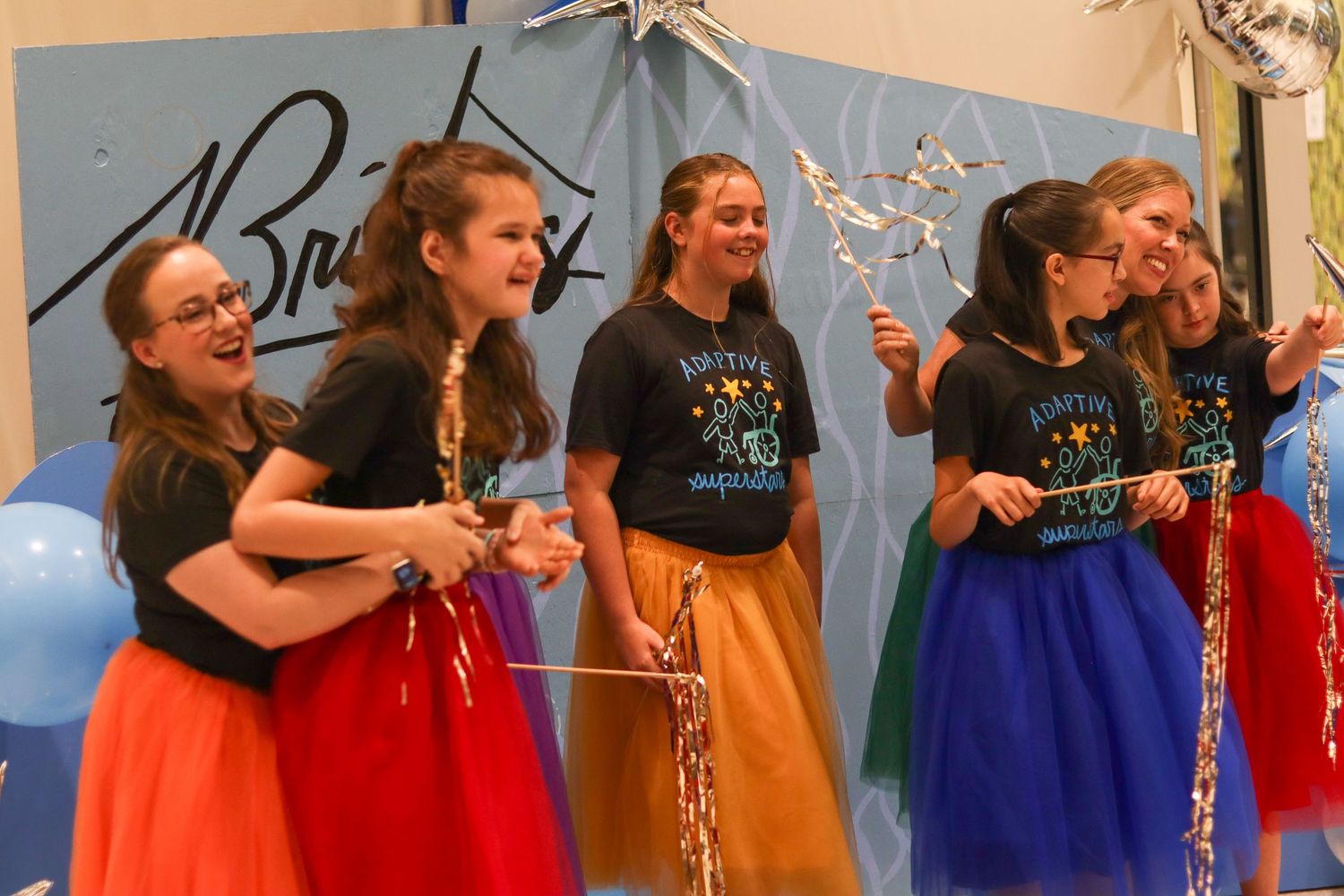 Five girls in colorful tulle skirts celebrate on stage with streamers at Bridges performance.