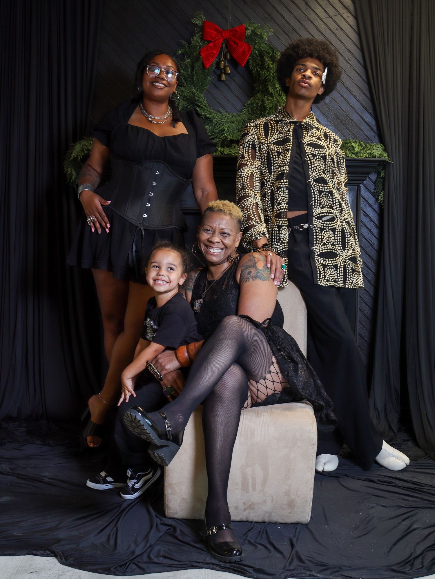 A family of four poses together in black outfits before a Christmas wreath backdrop.