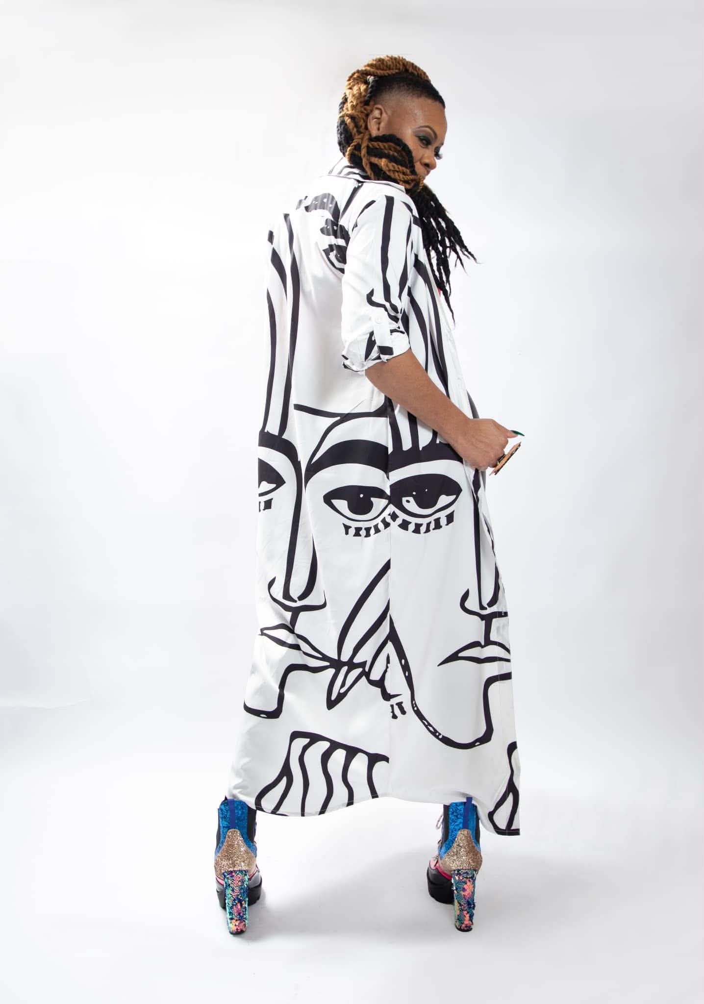 Woman with dreadlocks poses in a white abstract face-print maxi dress with colorful heels.