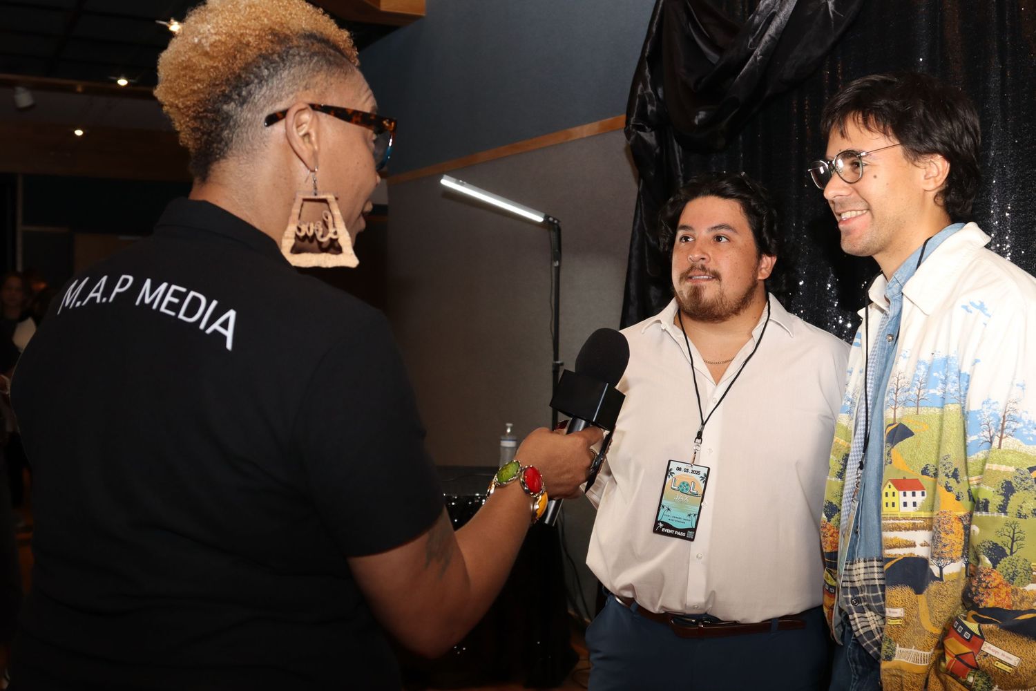 M.A.P. Media interviewer with microphone speaks to two guests at an indoor media event.