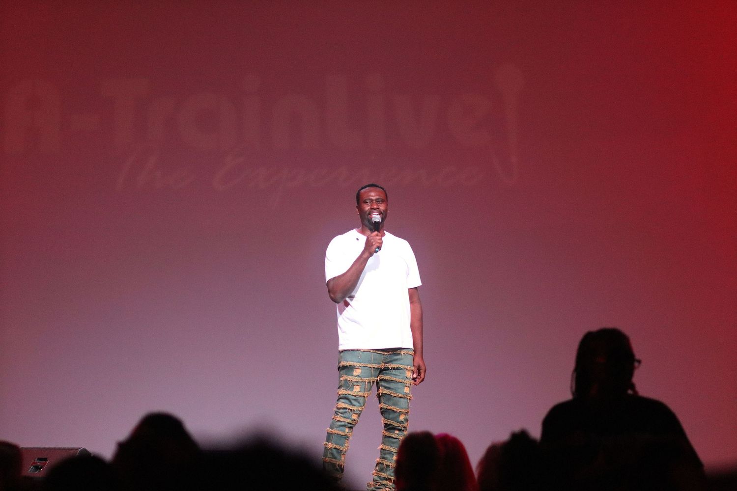 Performer in white shirt and camo pants on stage at A-Train Live The Experience event.