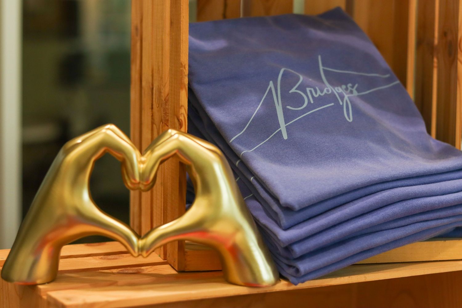 Gold heart-shaped hands sculpture beside folded blue shirts with signature at Bridges merchandise display.